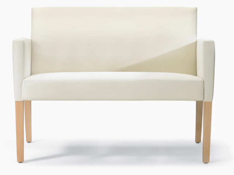 A front view of a Brava 862 plus chair in white textile with upholstered arms and maple legs.