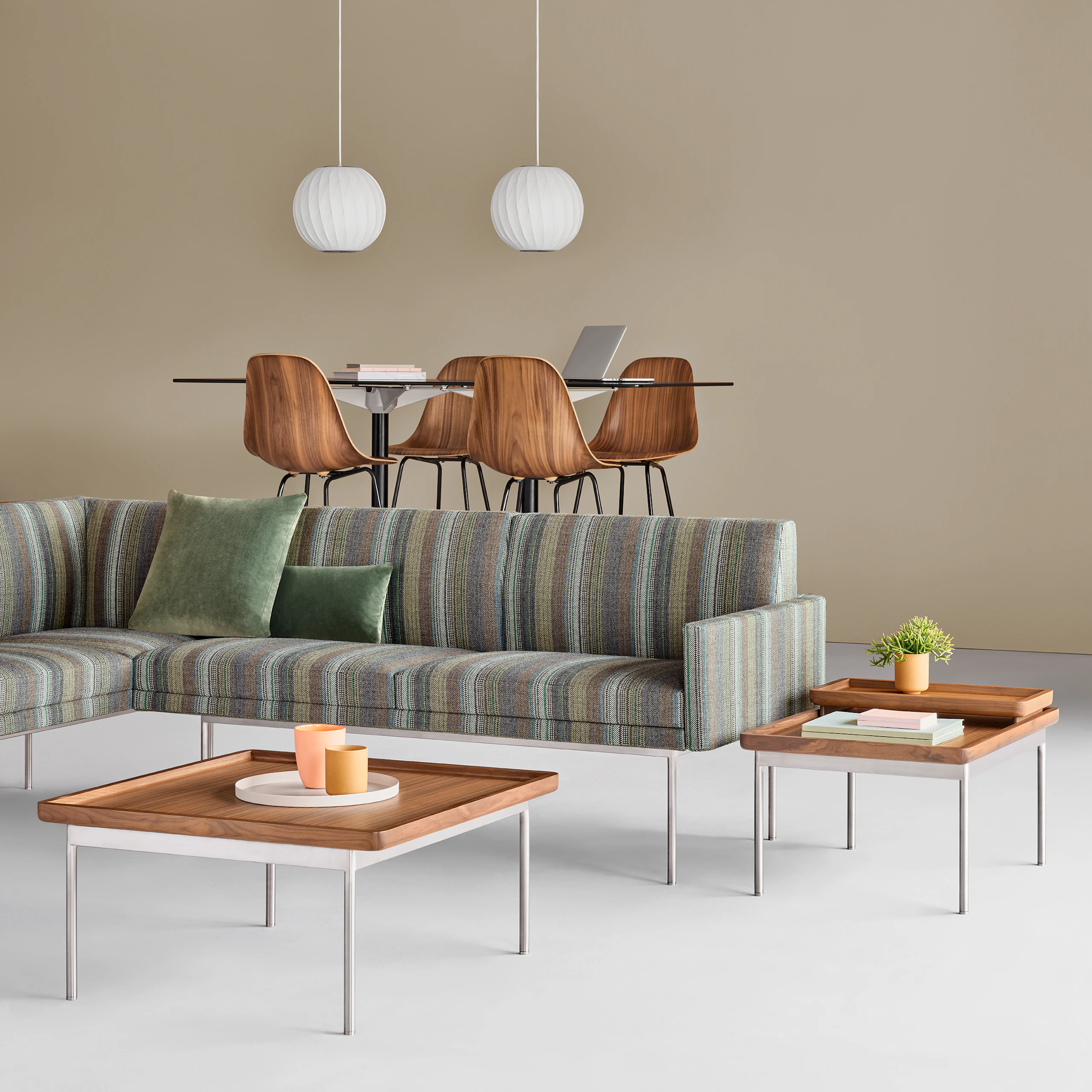 A lounge setting featuring a Tuxedo Sofa and two Tuxedo Tables. Four Eames Molded Wood Stools surround an Eames Table in the background.