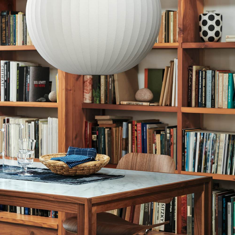 An Eames Molded Plywood Dining Chair with a metal base sits at a rectangular Doubleframe Table with bookshelves in the background.