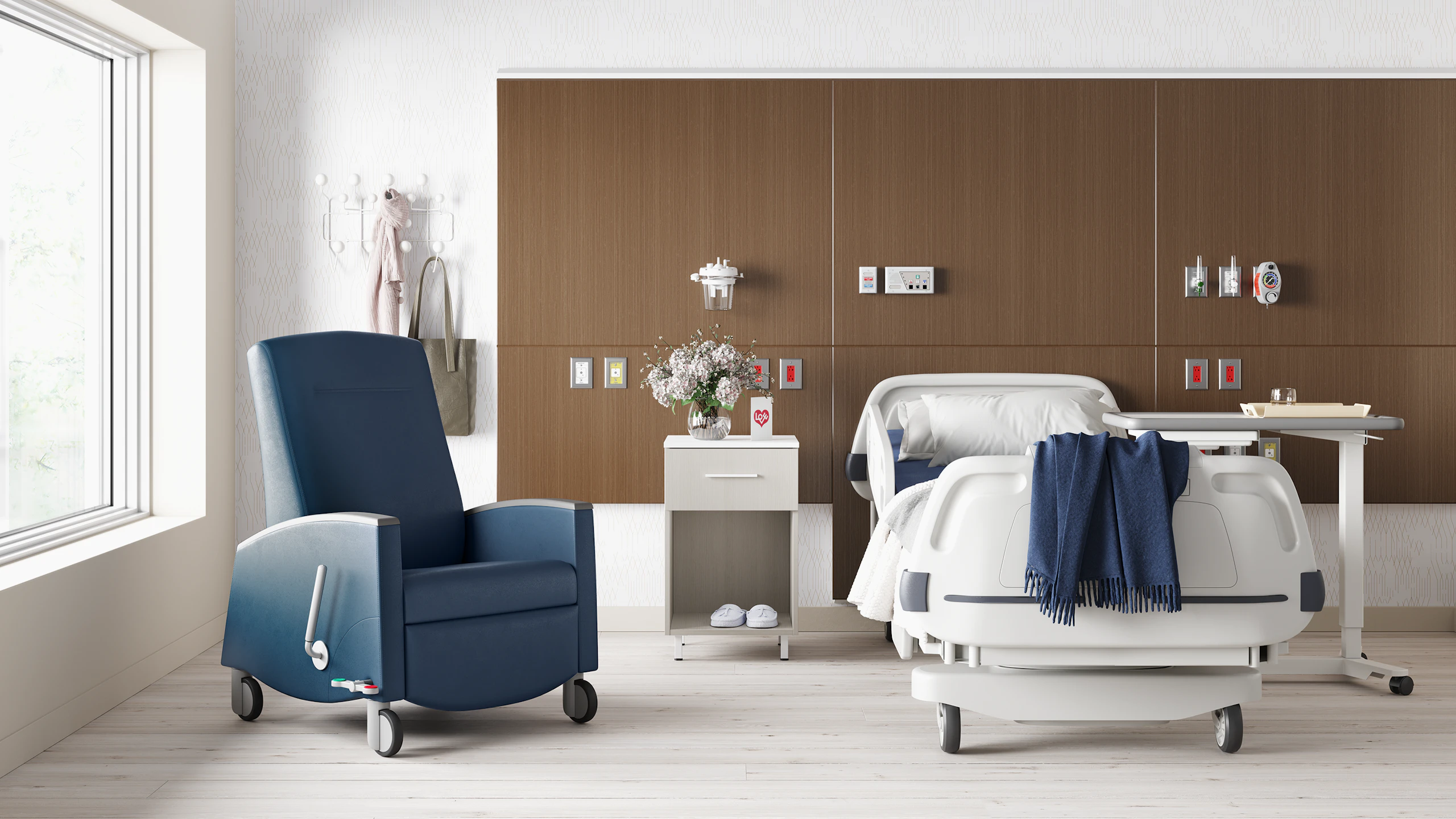 A patient room with a hospital bed in front of a headwall in a walnut finish with a Nemschoff Bedside Cabinet and Sahara Recliner next to it and an EZ-123 Overbed Table on the other side.
