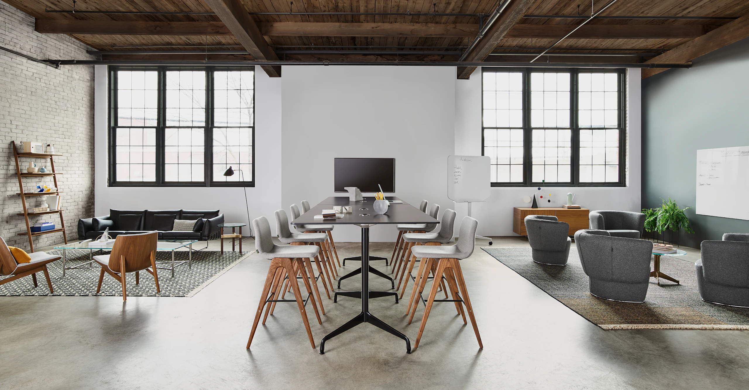 Eight light grey Viv Wood Stools around two rectangular black Eames Standing Height Tables. The scene is set in between two lounge areas in front of a white wall with large windows.