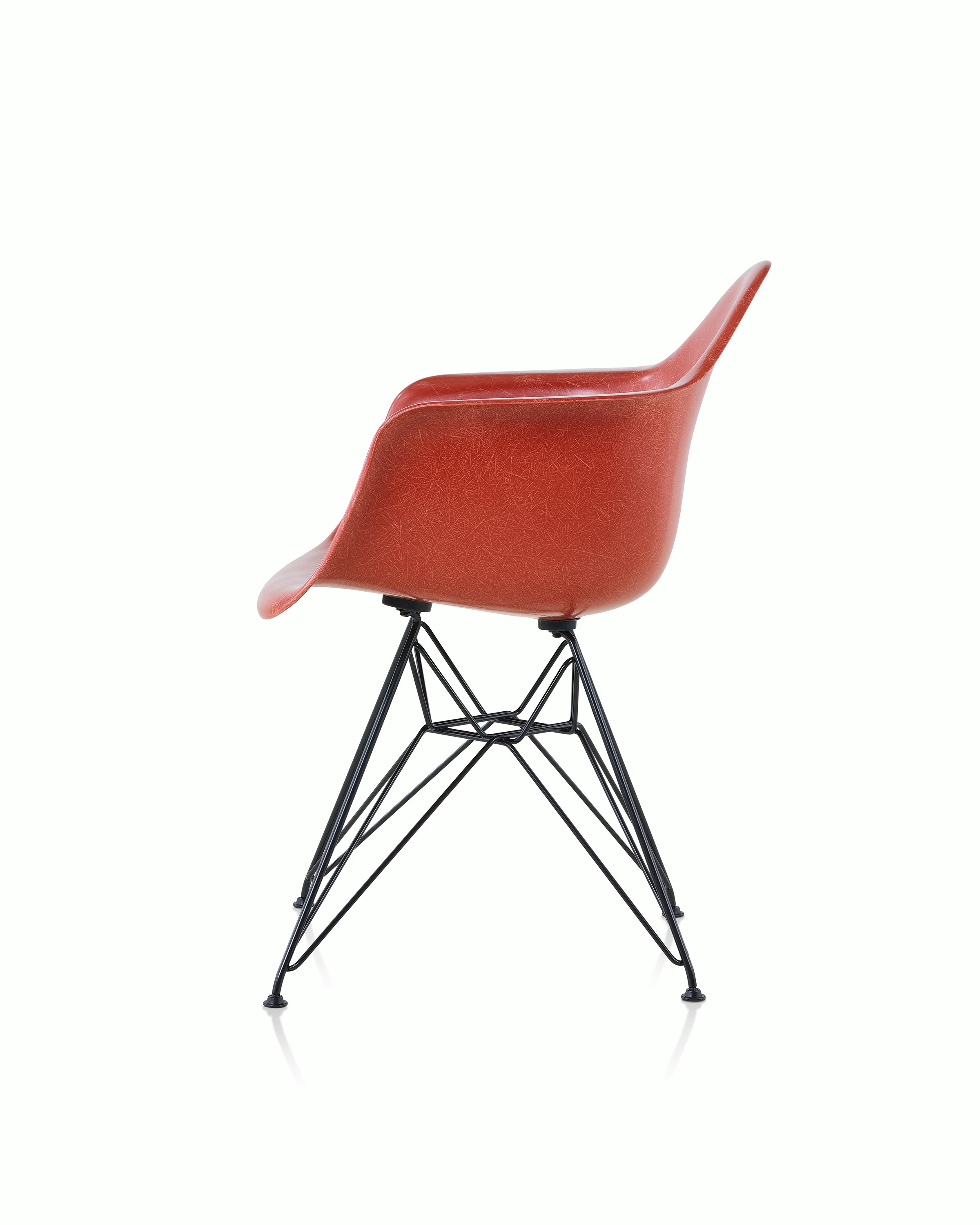 A red Eames Molded Fiberglass Chair with arms and a wire base, viewed from the side.
