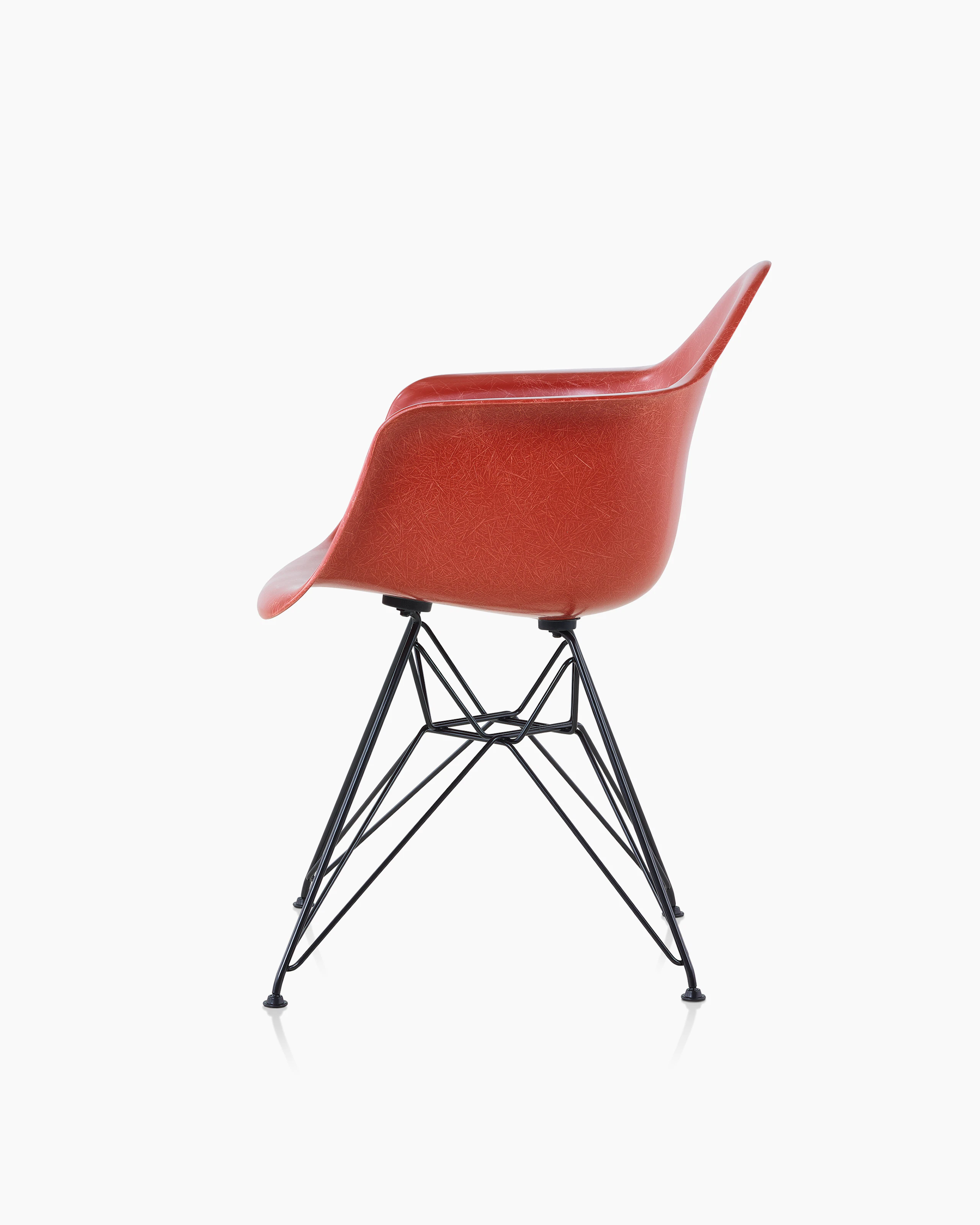A red Eames Molded Fiberglass Chair with arms and a wire base, viewed from the side.