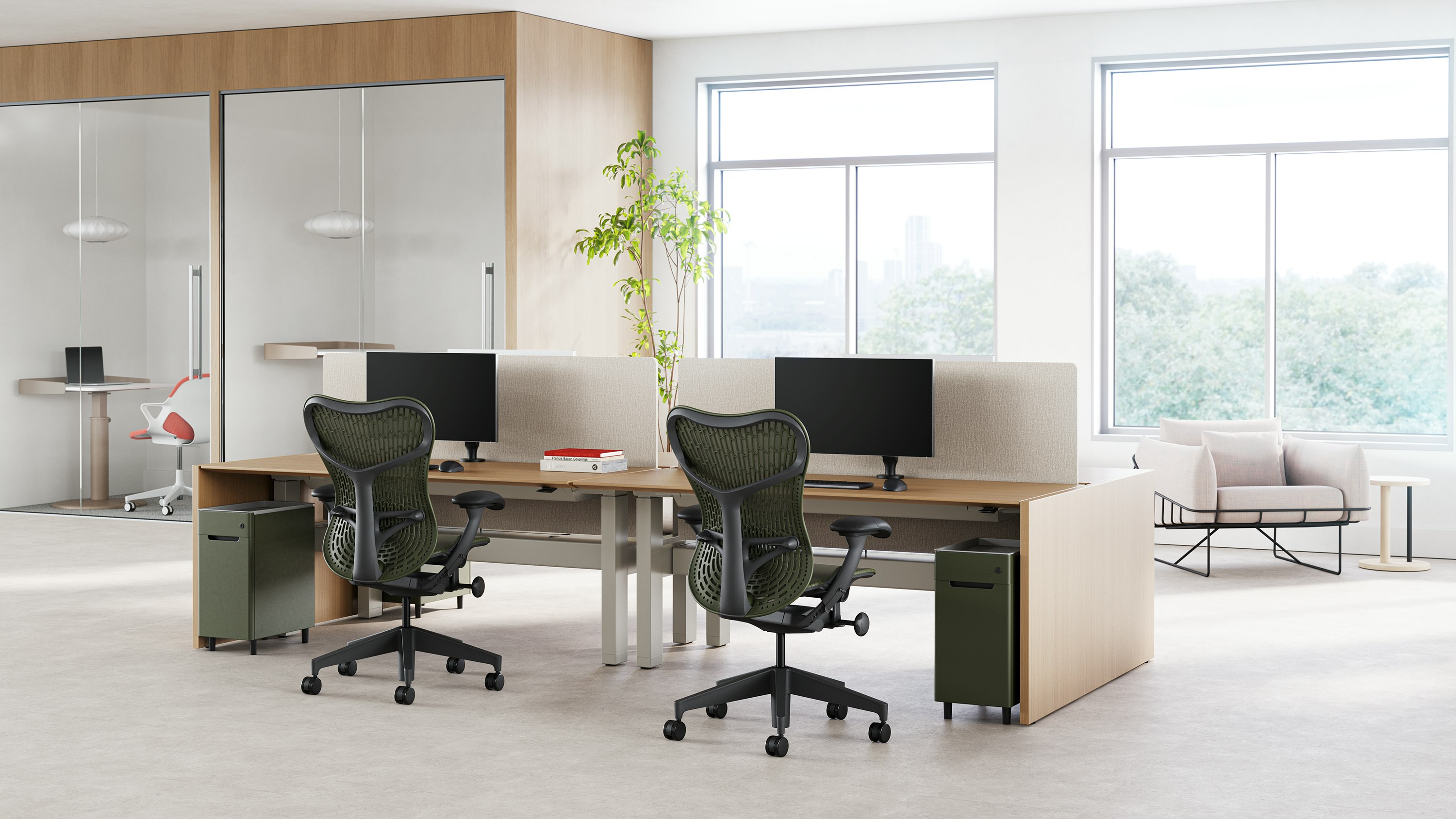 Two Mirra 2 chairs in with a graphite frame and olive butterfly back sit in front of a workstation in a touchdown space, with a room in the background.