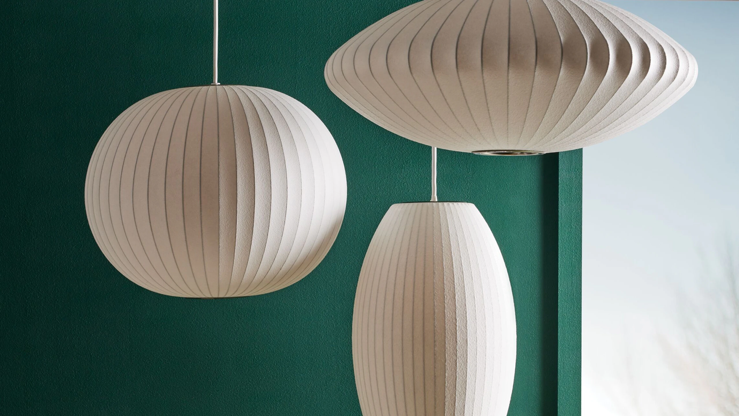 A Nelson Ball Pendant Lamp, Nelson Cigar Bubble Pendant, and Nelson Saucer Bubble Pendant hanging in front of a green wall