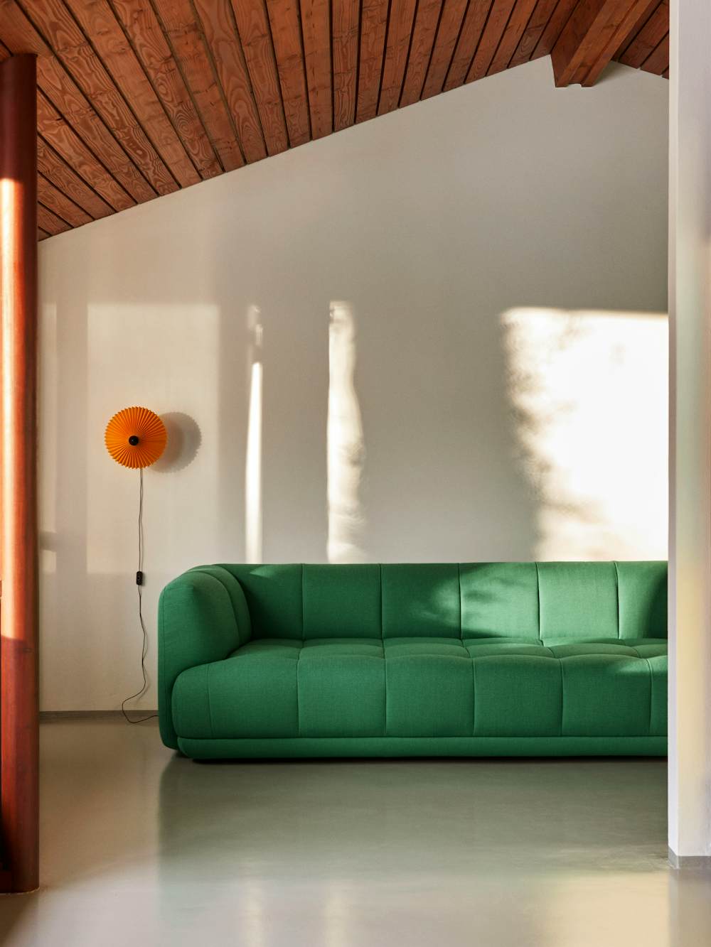A living space with a green Quilton Sofa and Matin Flushmount Light by Hay.​