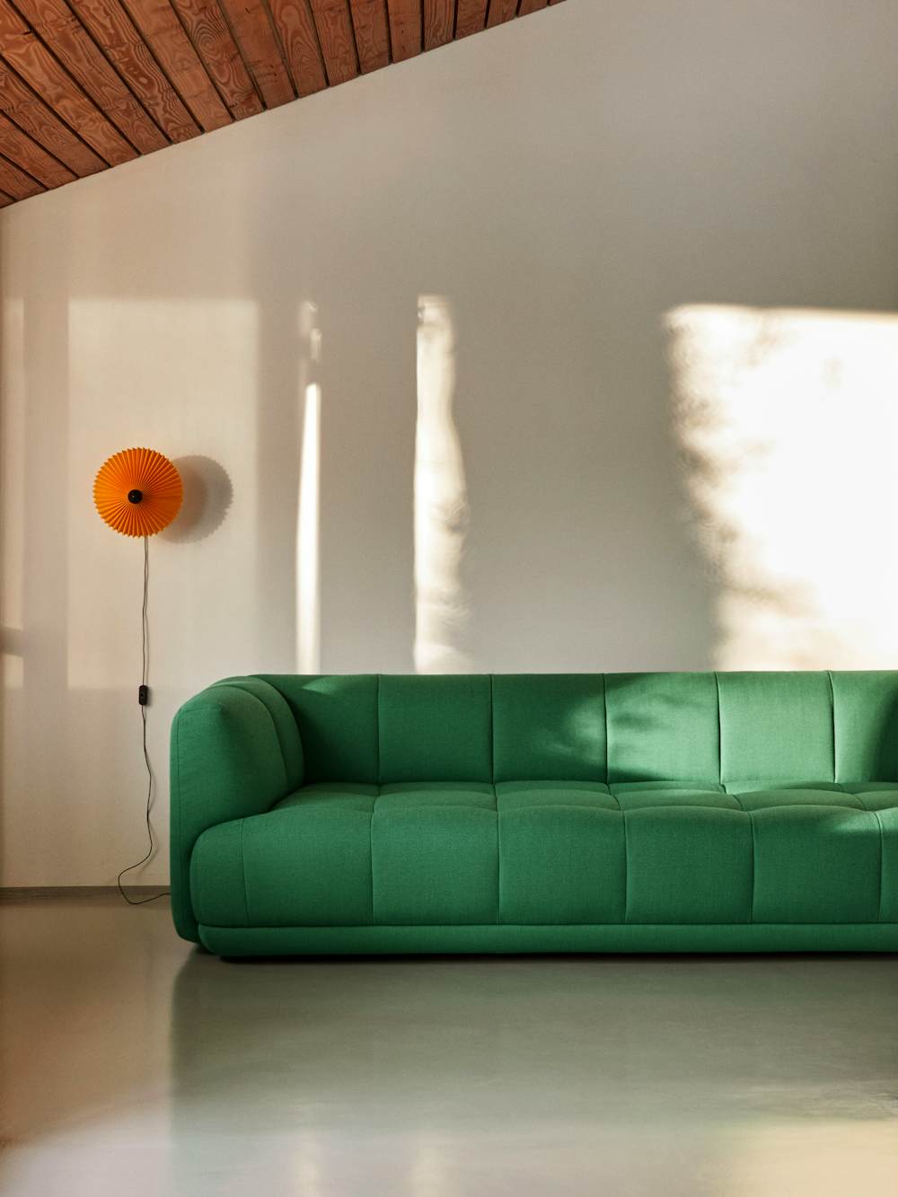 A living space with a green Quilton Sofa and Matin Flushmount Light by Hay.