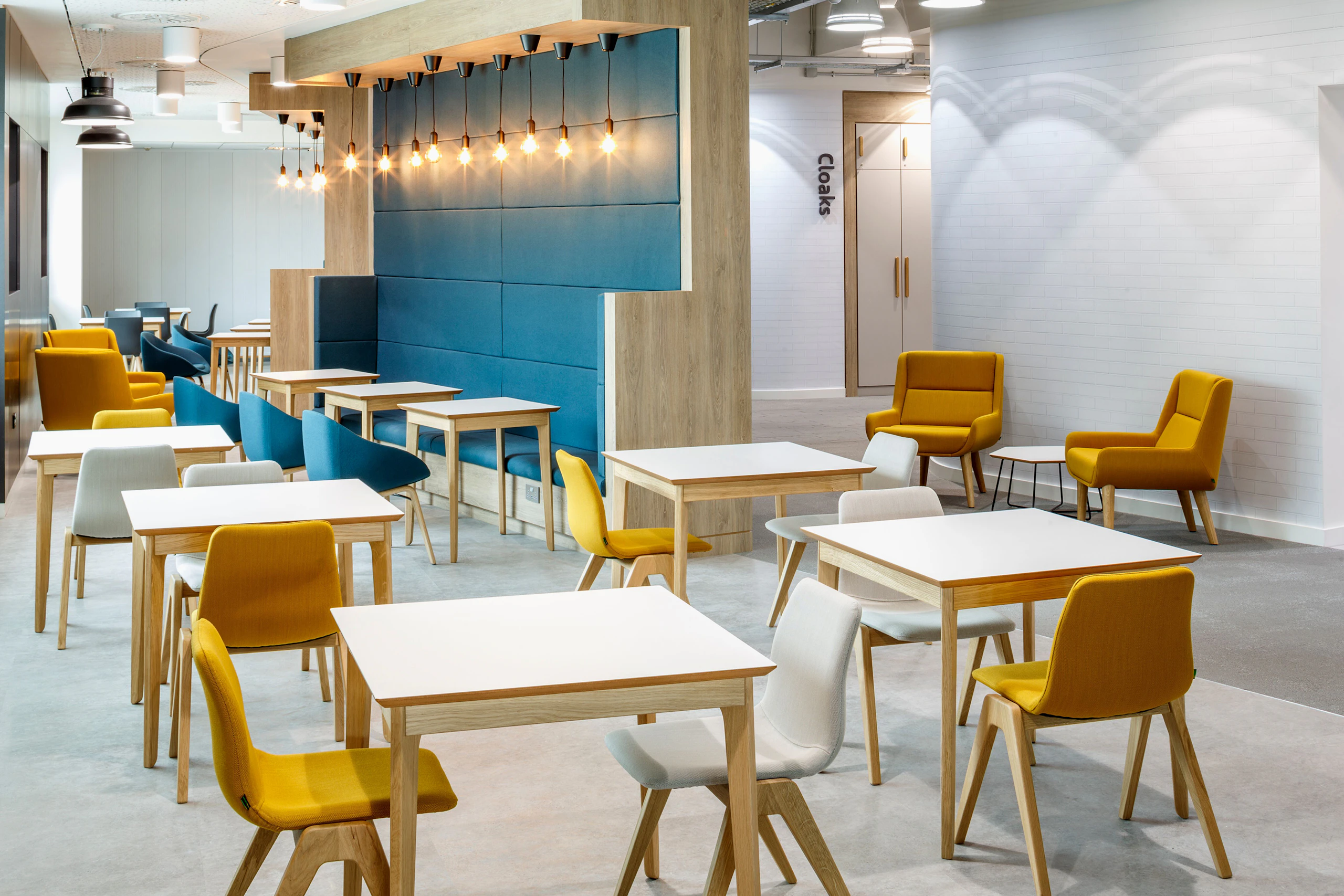 A bright cafe or cafeteria space full of white naughtone Dalby Café Tables arranged with cream and gold Viv Wood Chairs and blue Always Side Chairs.
