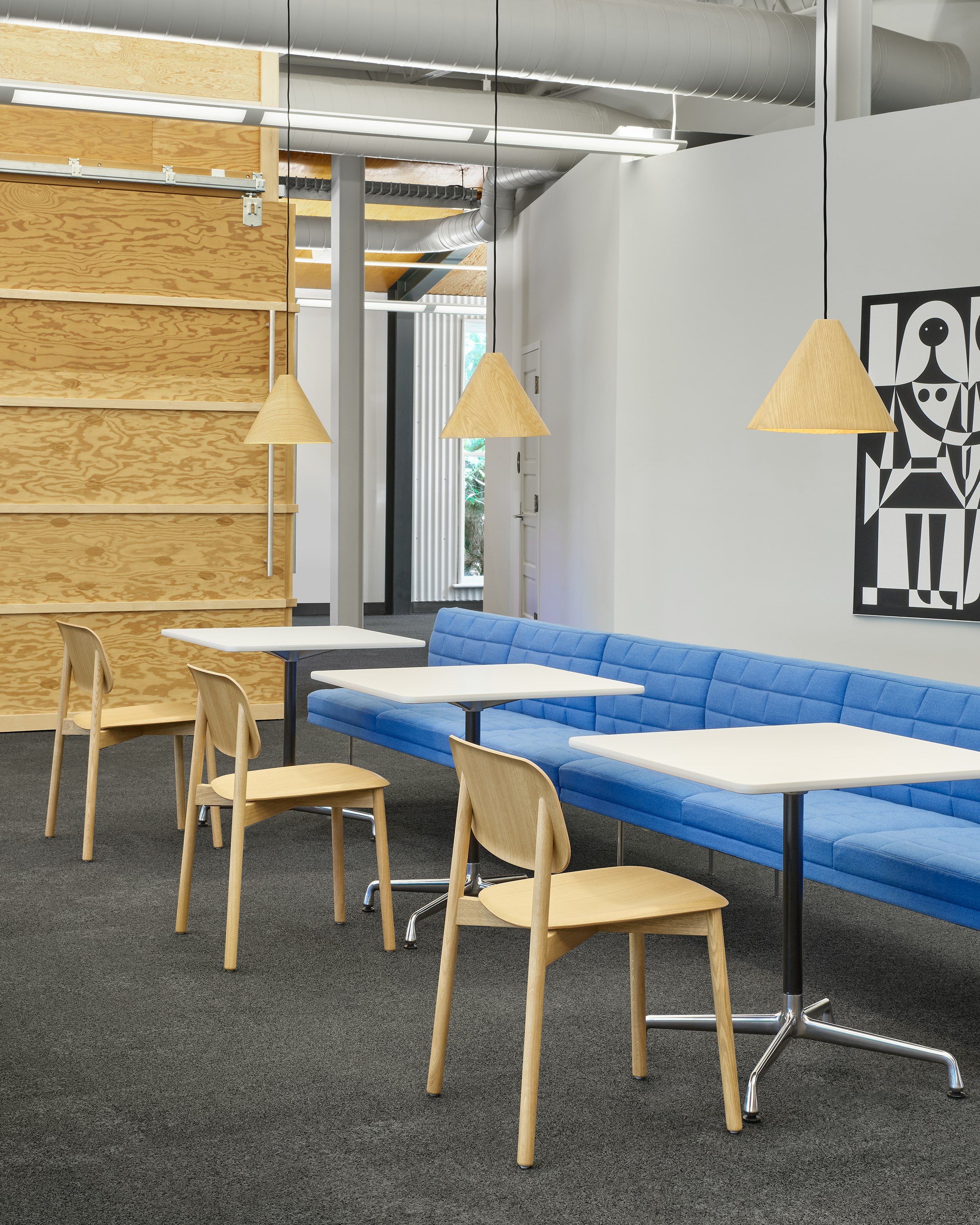 A Blue Tuxedo Component Lounge Sofa next to three Eames Conference tables and three Oak Soft Edge Chairs in an open plaza space.