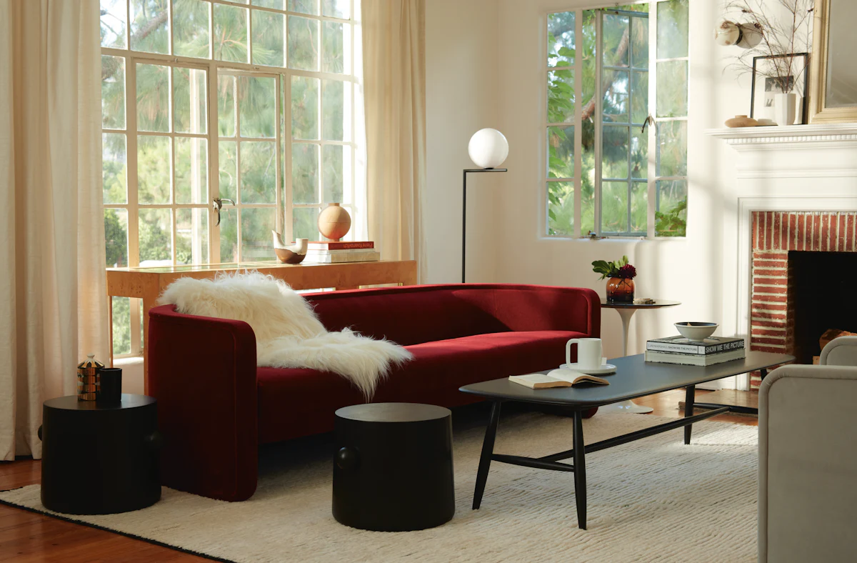 Bright living room with red sofa by a fireplace and grey chairs, large windows