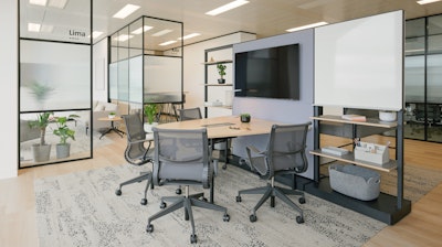 Four Setu Chairs by Herman Miller arranged around an OE1 Huddle Table in front of a TV mounted on a shelving system