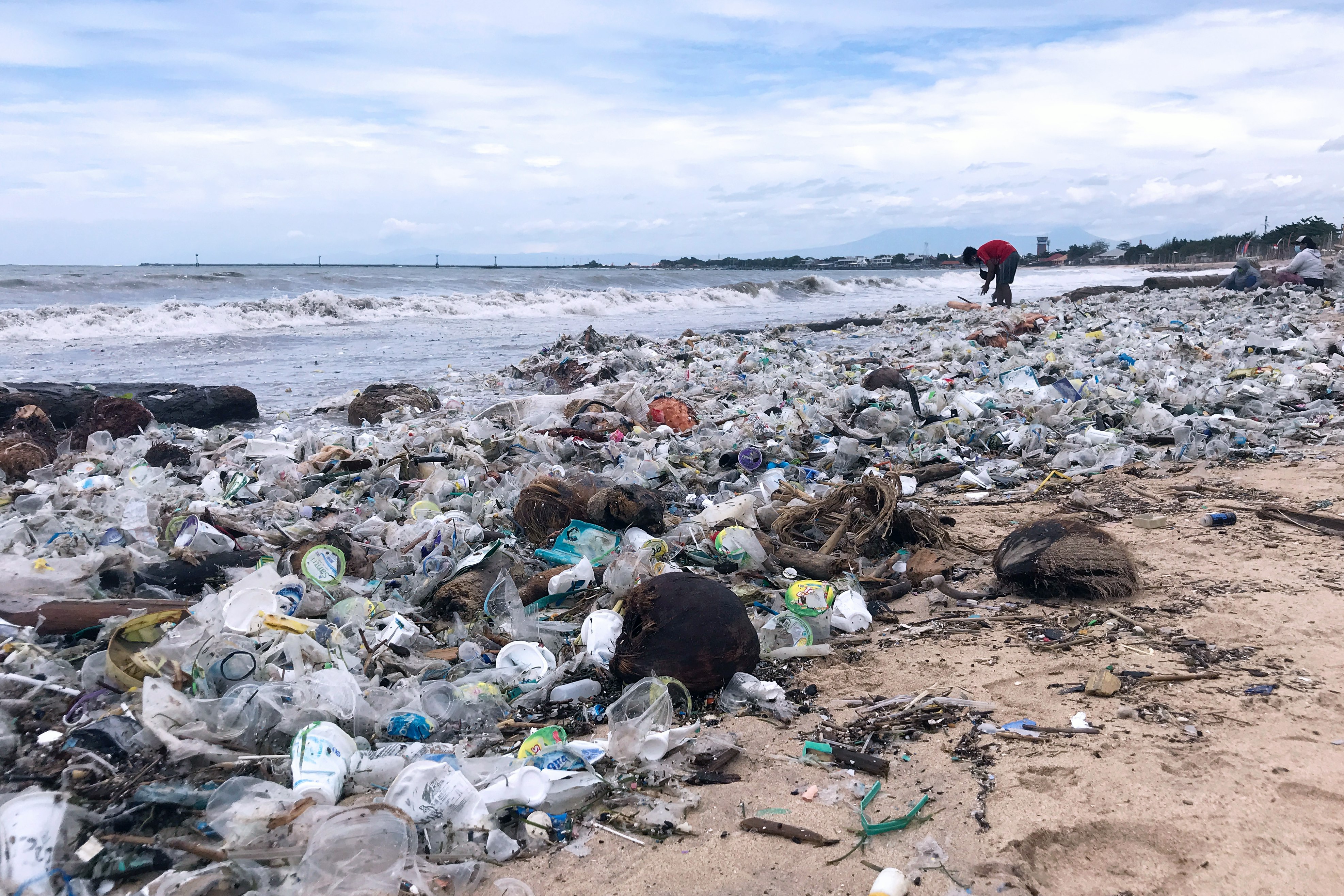 A person I picking up trash on a beach littered with plastic trash.