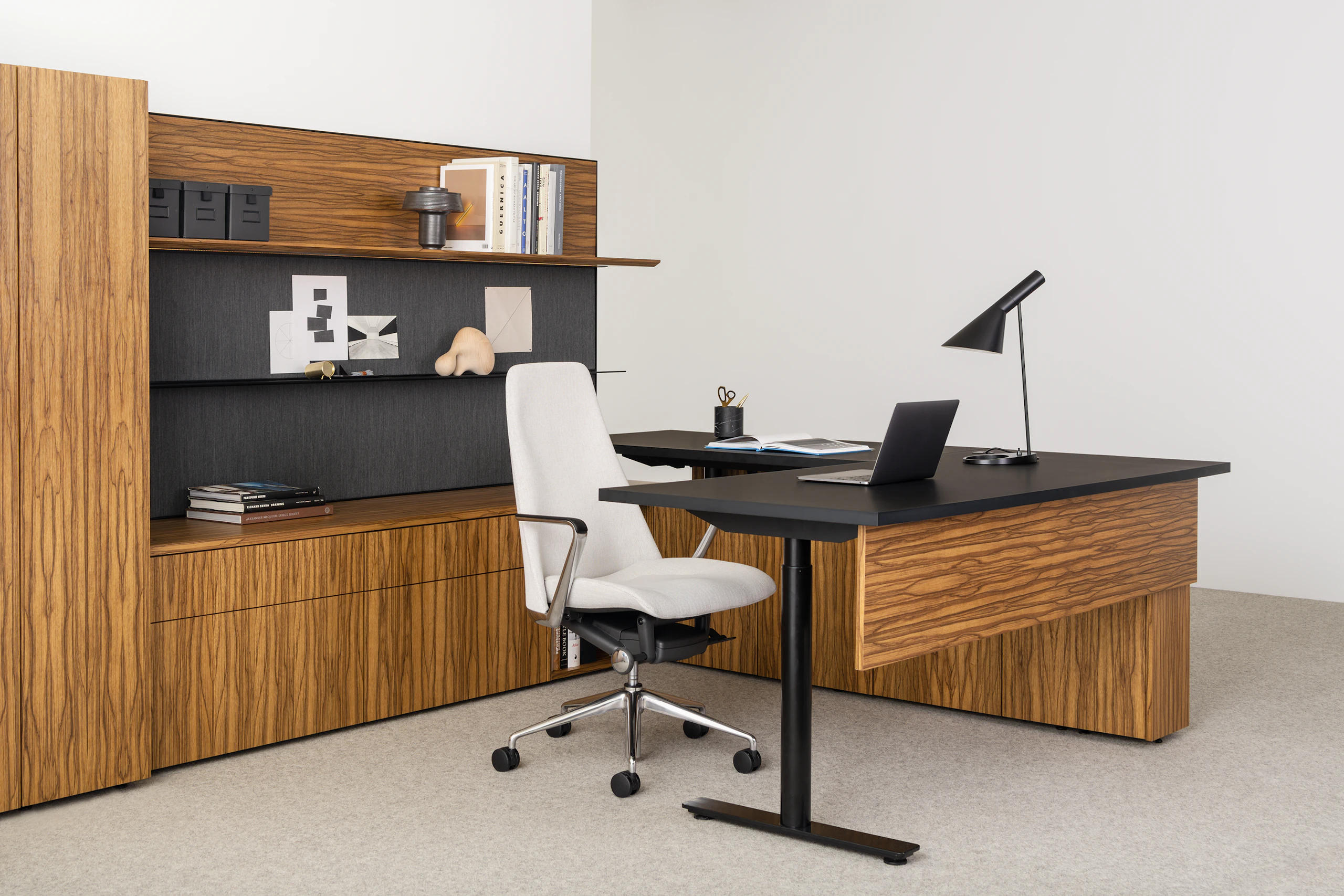 A U-shaped executive office featuring wood-paneled casegoods, a white leather Taper Chair, and a height-adjustable desk. Black limba flat matte book matched.