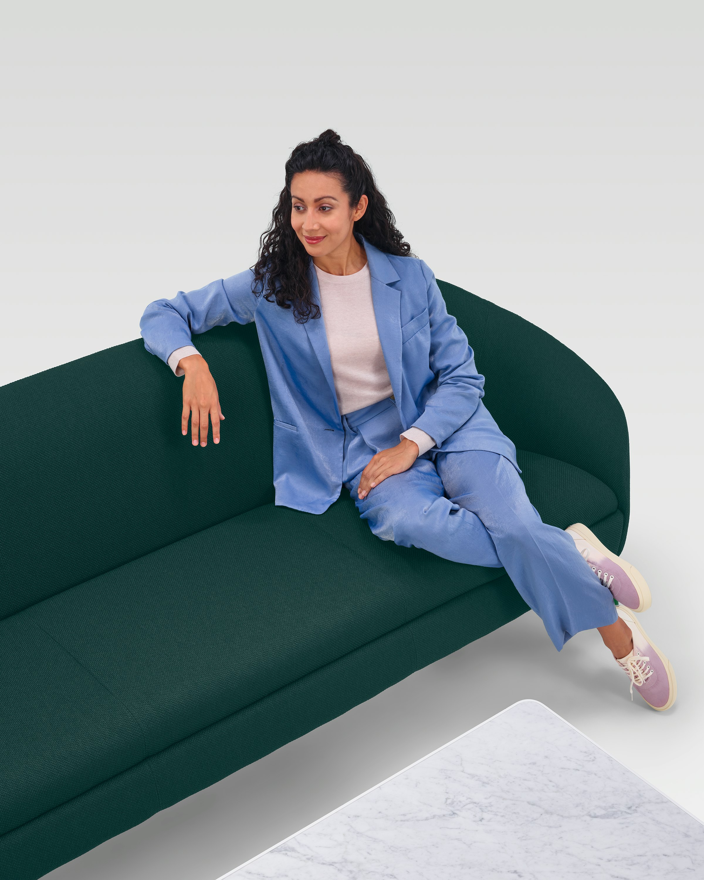 A woman sitting on a dark green three-seat Ever Sofa near a marble coffee table.