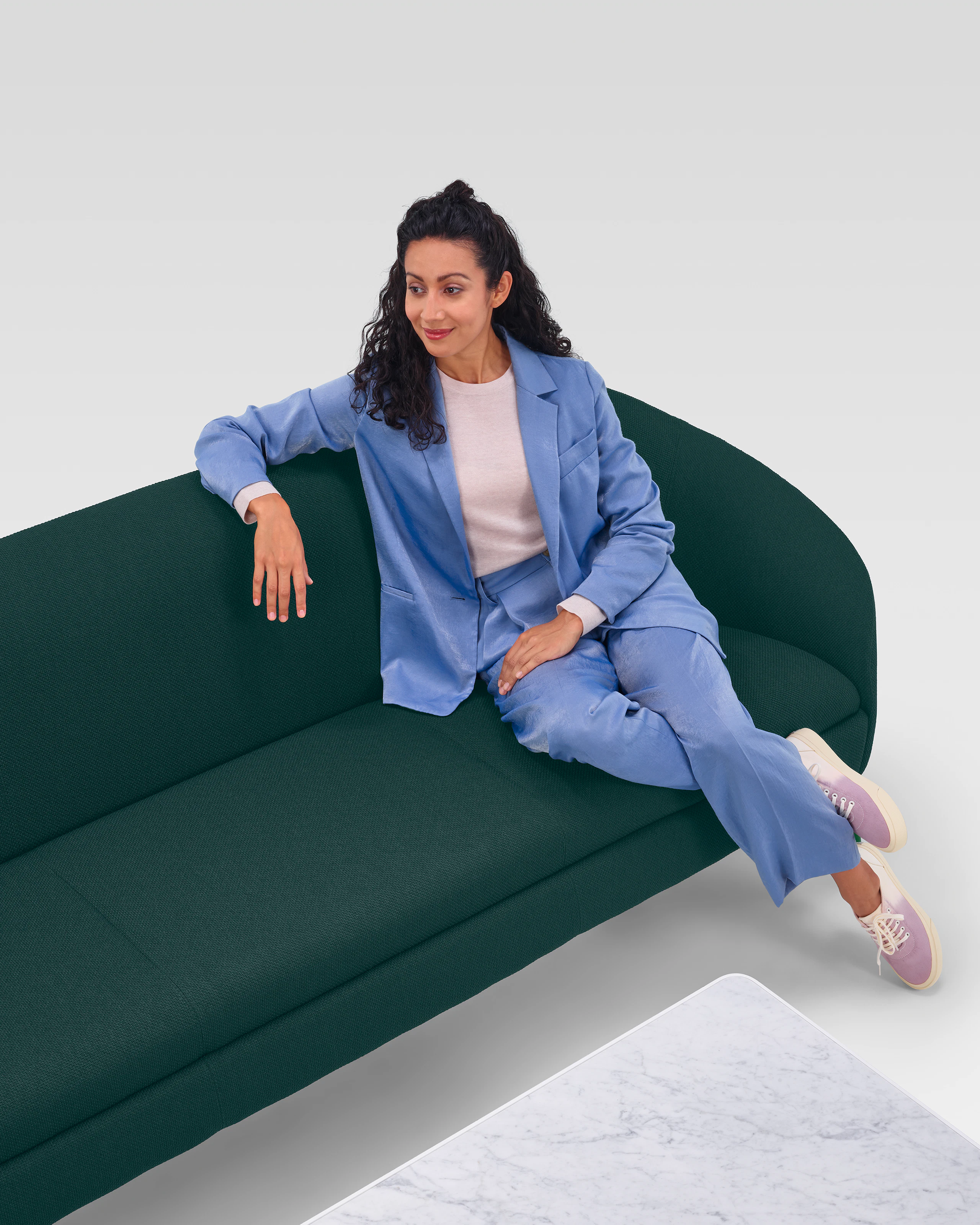 A woman sitting on a dark green three-seat Ever Sofa near a marble coffee table.