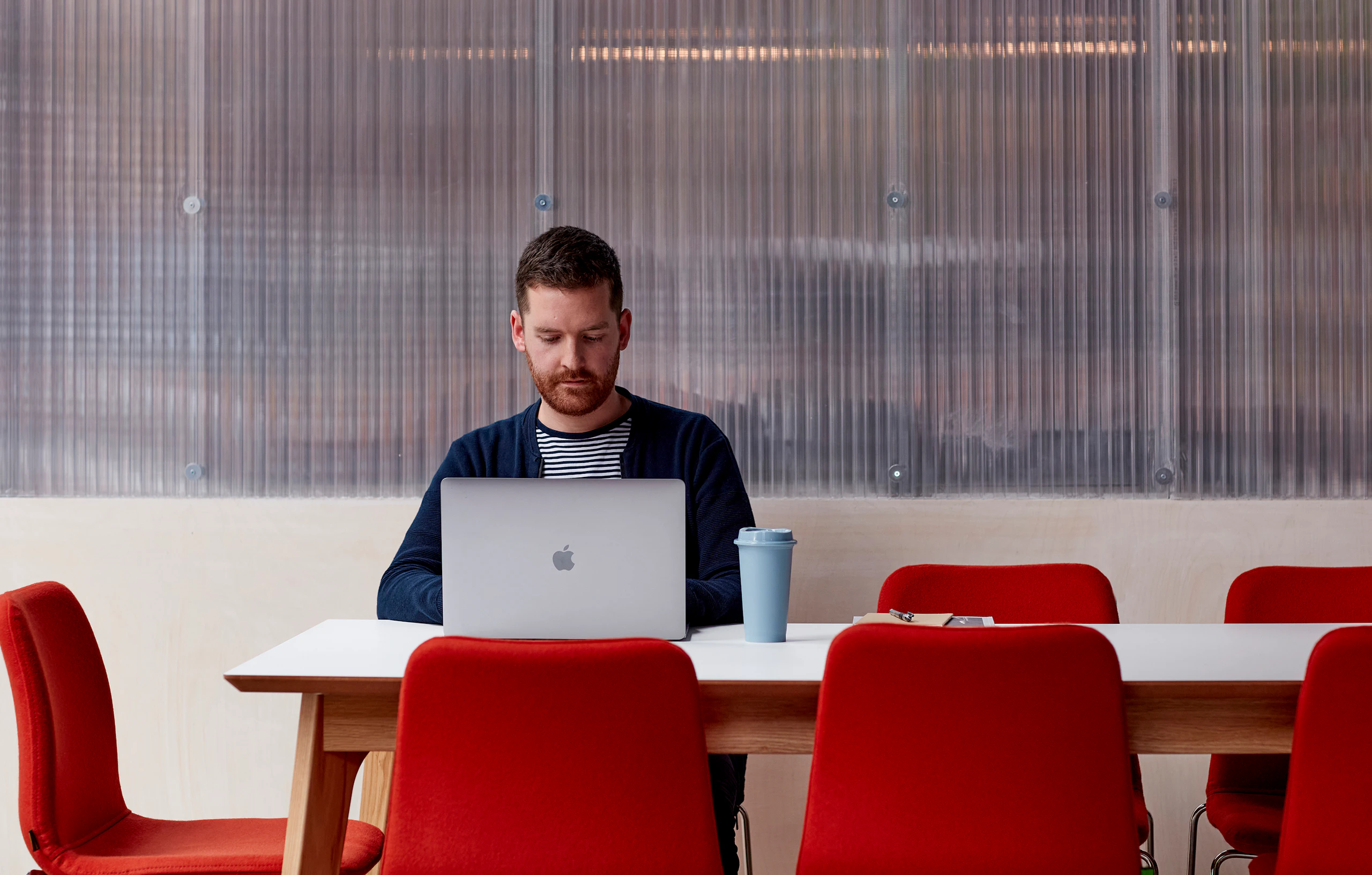 A man working on a laptop at a white Dalby table with 8 red Viv chairs around the table.