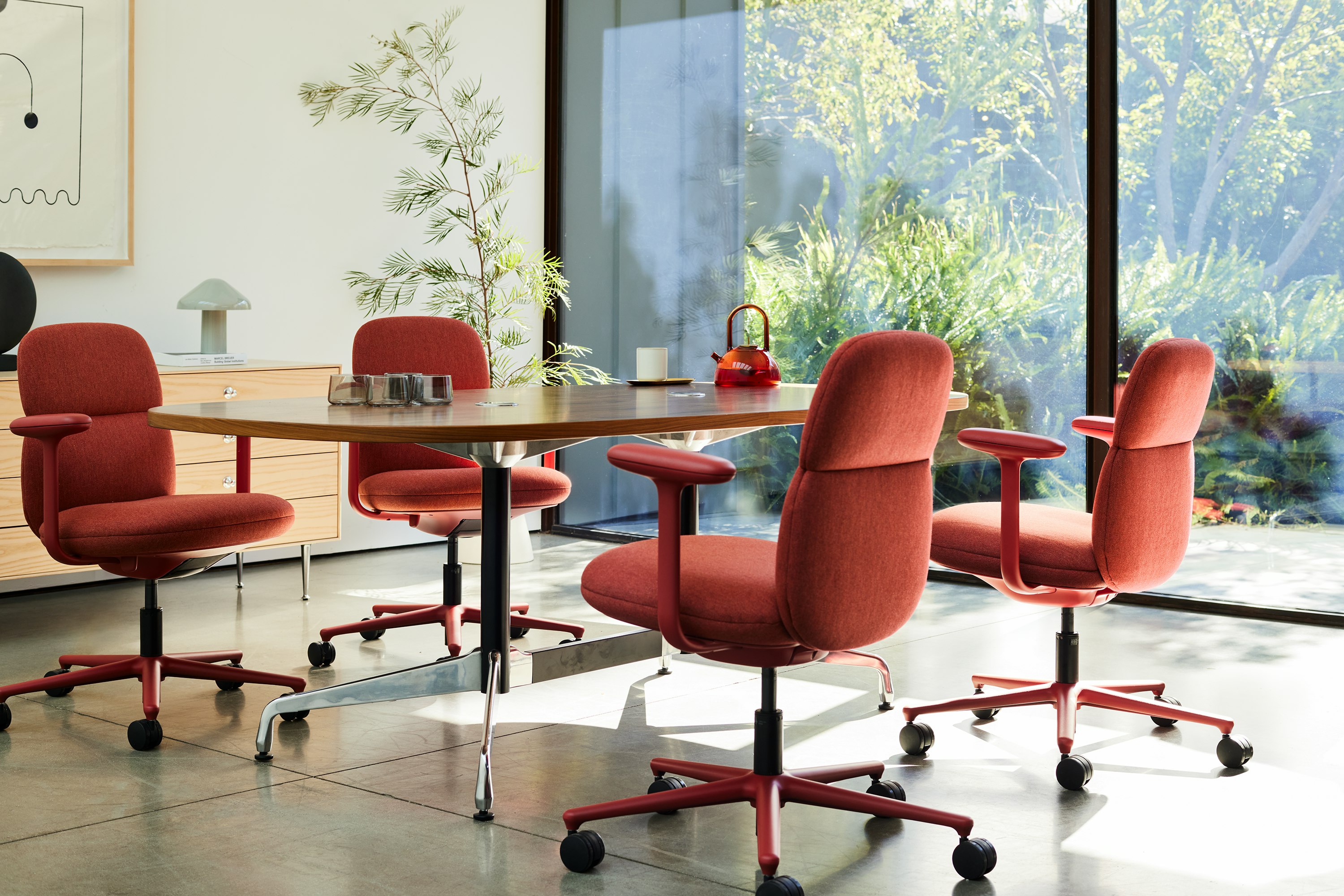 Four Asari chairs by Herman Miller in deep red surround a table in a room next to a sunny window.