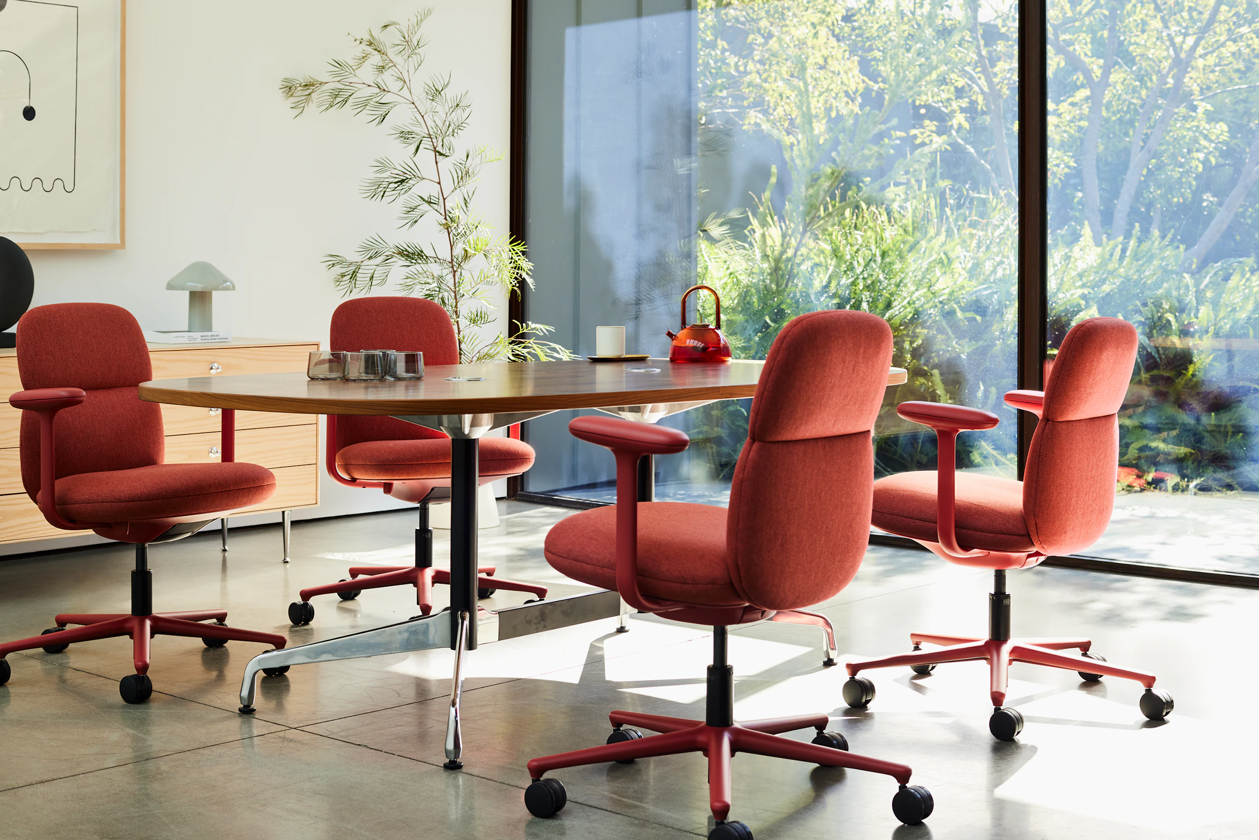 Four Asari chairs by Herman Miller in deep red surround a table in a room next to a sunny window.