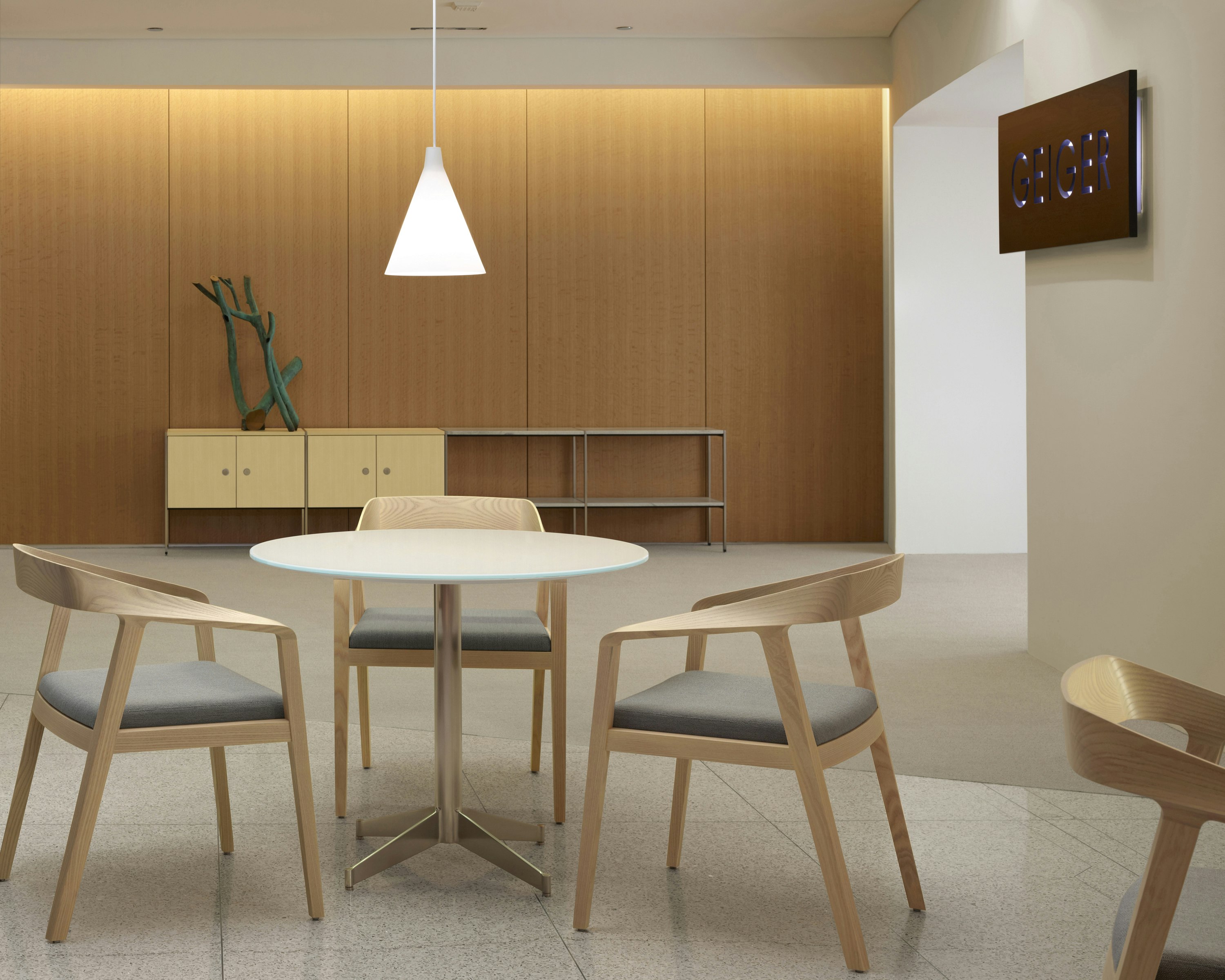 An interaction space with three Full Twist Guest Chairs around a table in the foreground and an H Frame Storage credenza against the back wall.