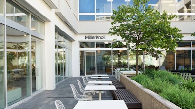 Several white Eames Wire Chairs by Herman Miller arranged at tables next to green foliage outside the MillerKnoll Dallas showroom