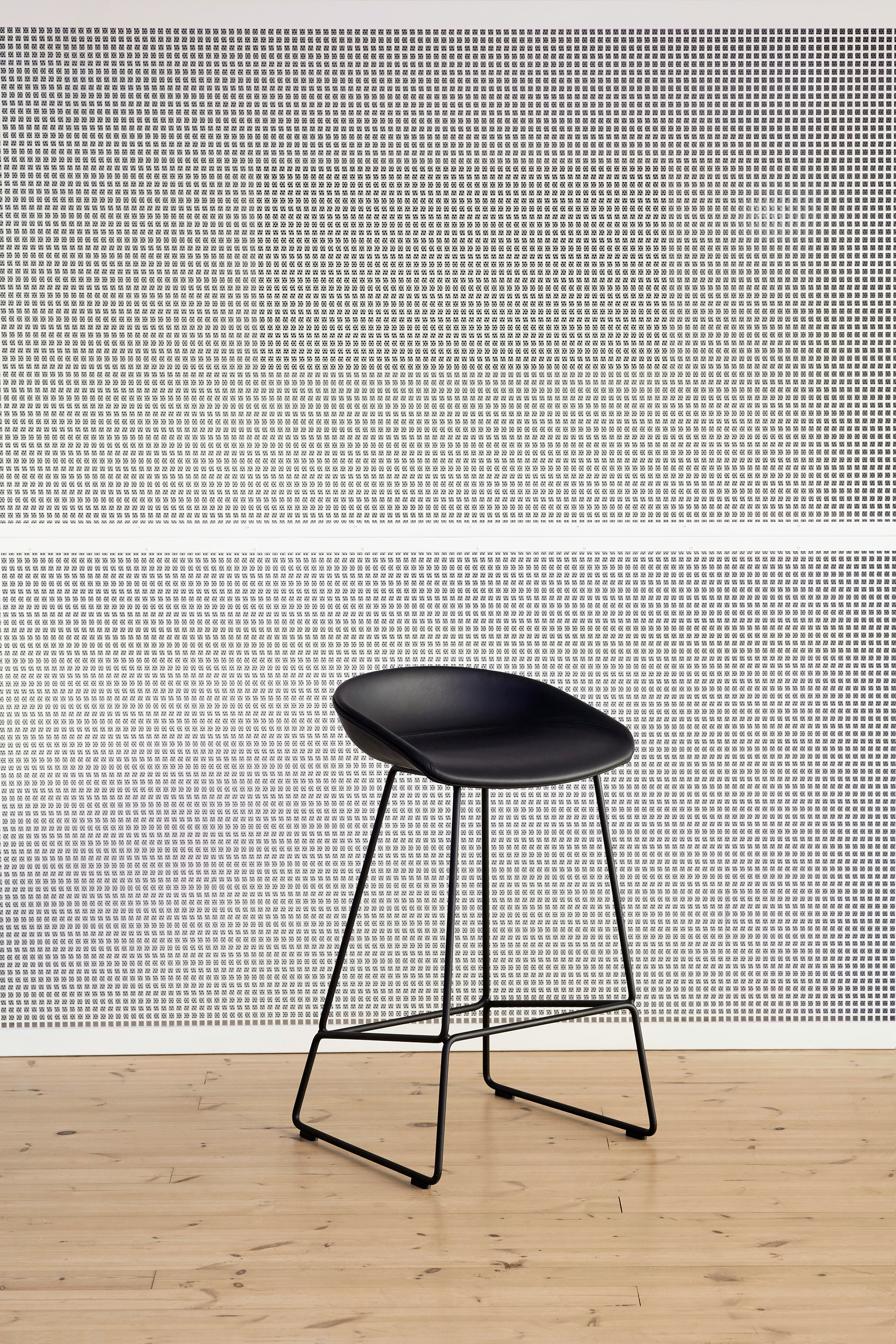 Black About A Stool, standing against wall alone, viewed at an angle.