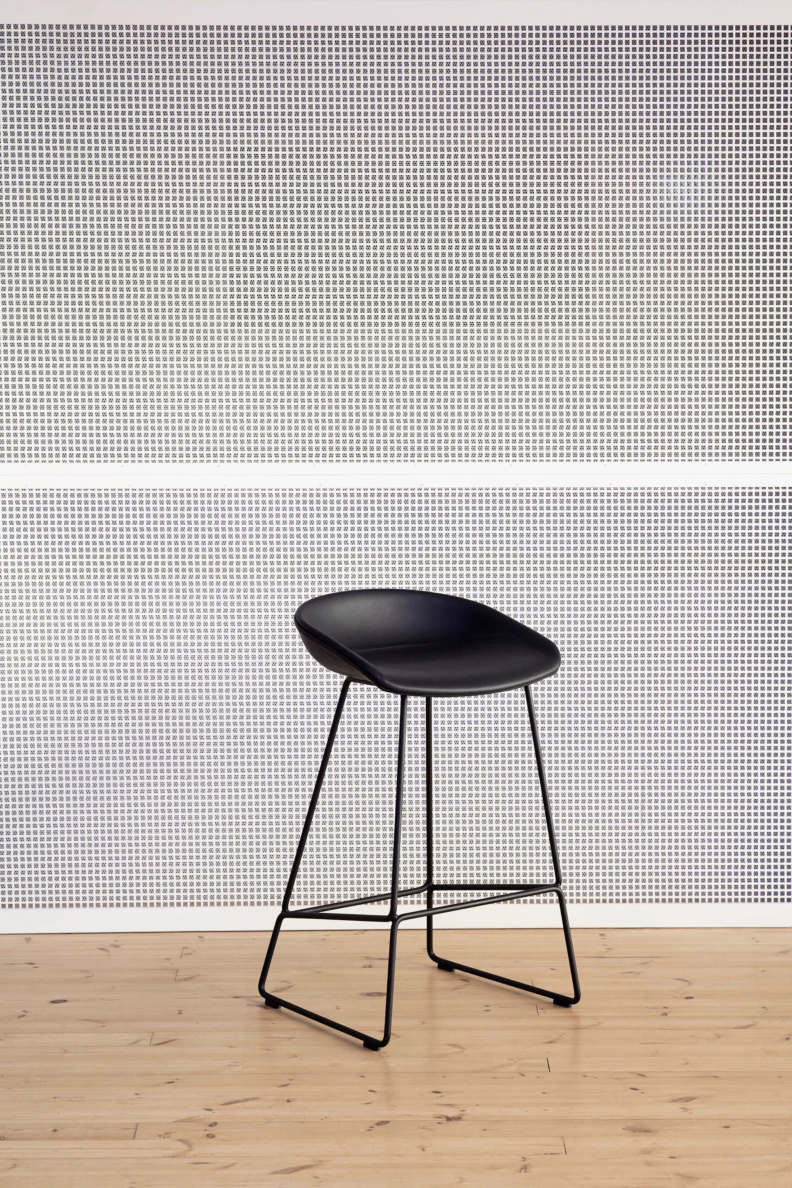 Black About A Stool, standing against wall alone, viewed at an angle.