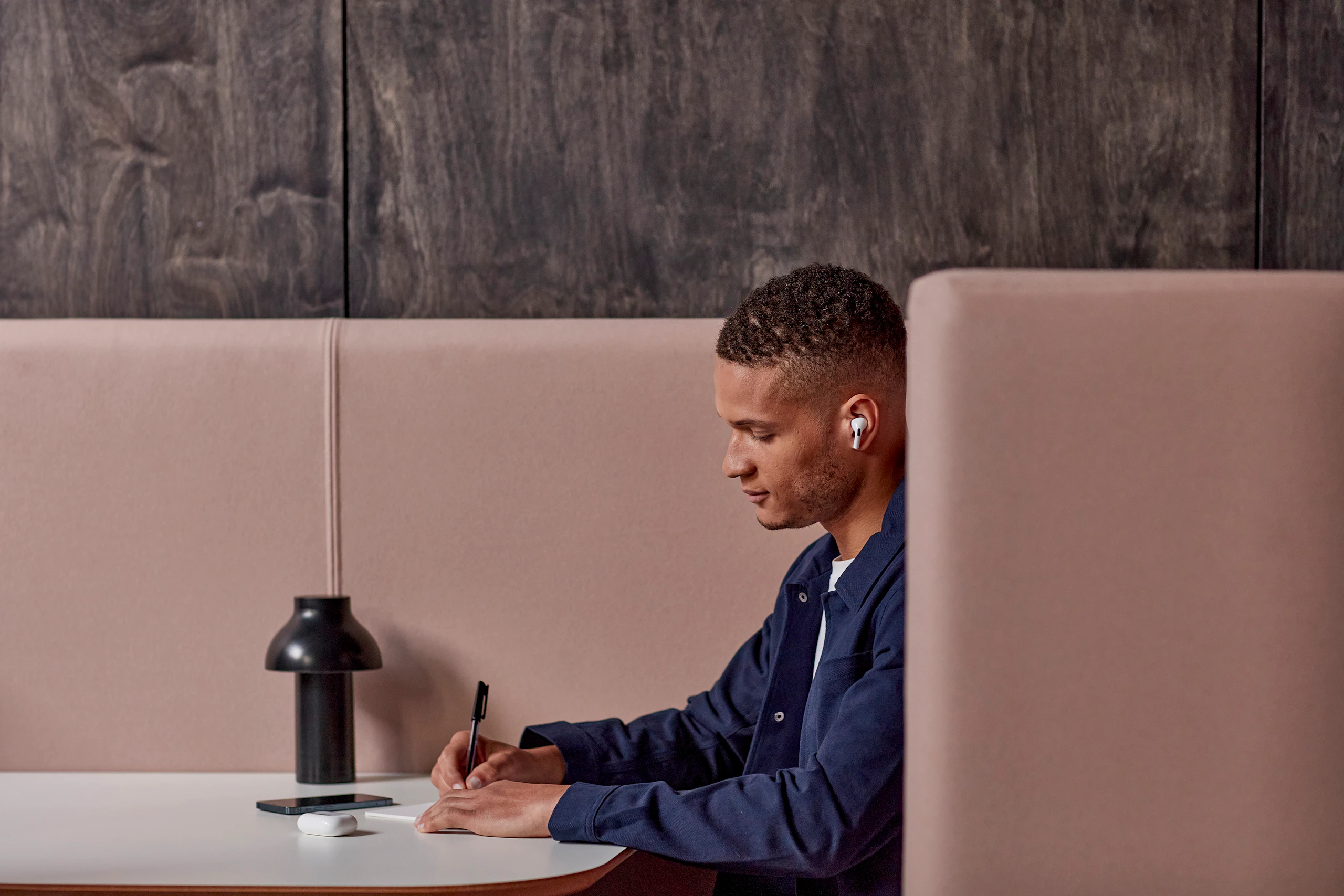 Man sitting within pale pink Pullman booth with white table top and oak legs.