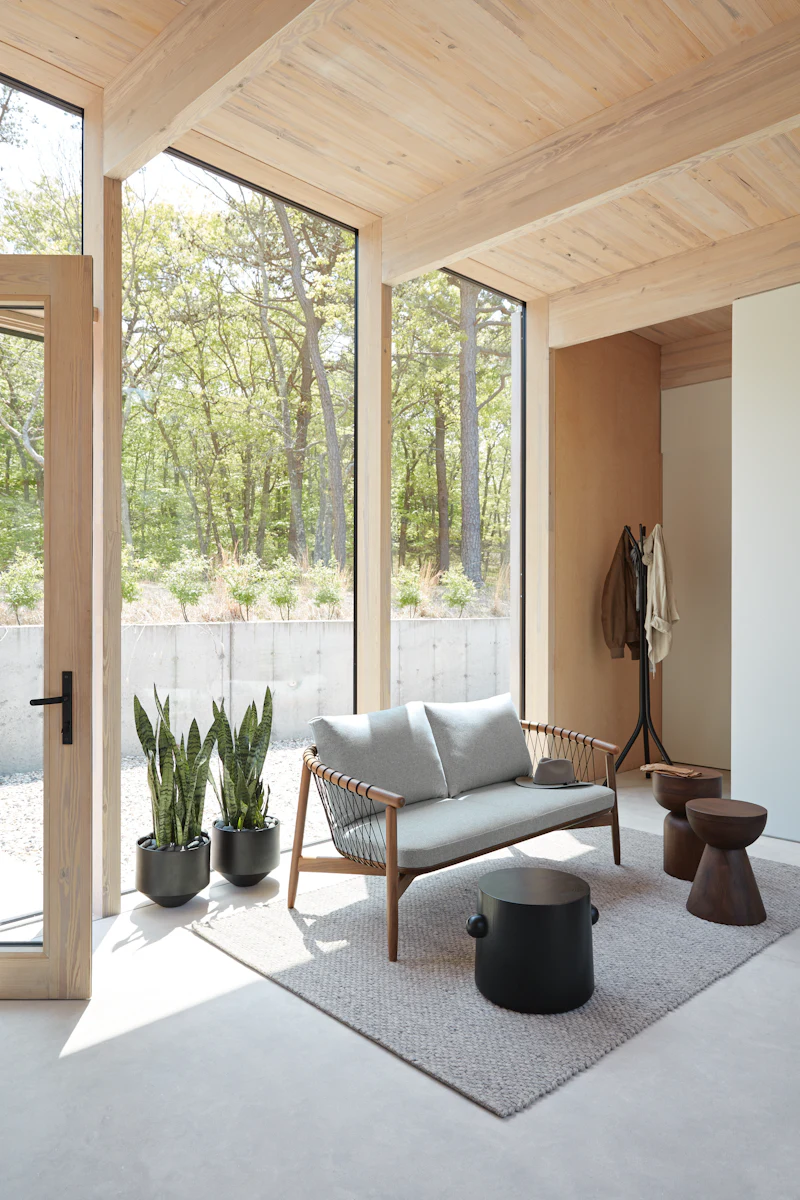 Bright sunlit living space with large windows, wood ceiling, and indoor seating area with plants