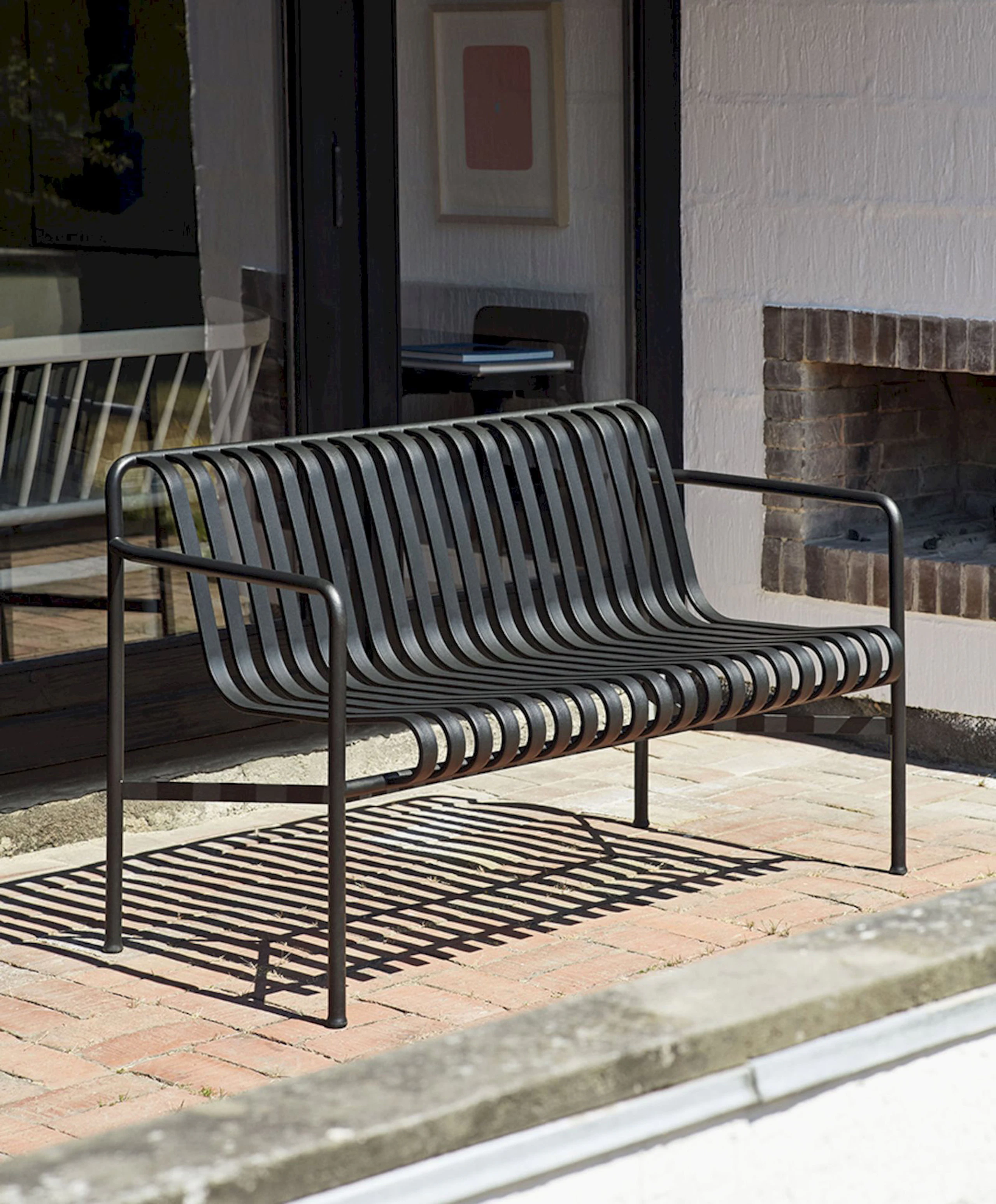 A Palissade Dining Bench is dark grey sits on a patio next to an outdoor fireplace.