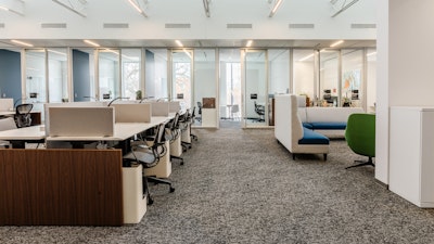 Research institute workplace showing a row of height adjustable desks, wiith lounge seating nearby, and individual offices at the back.