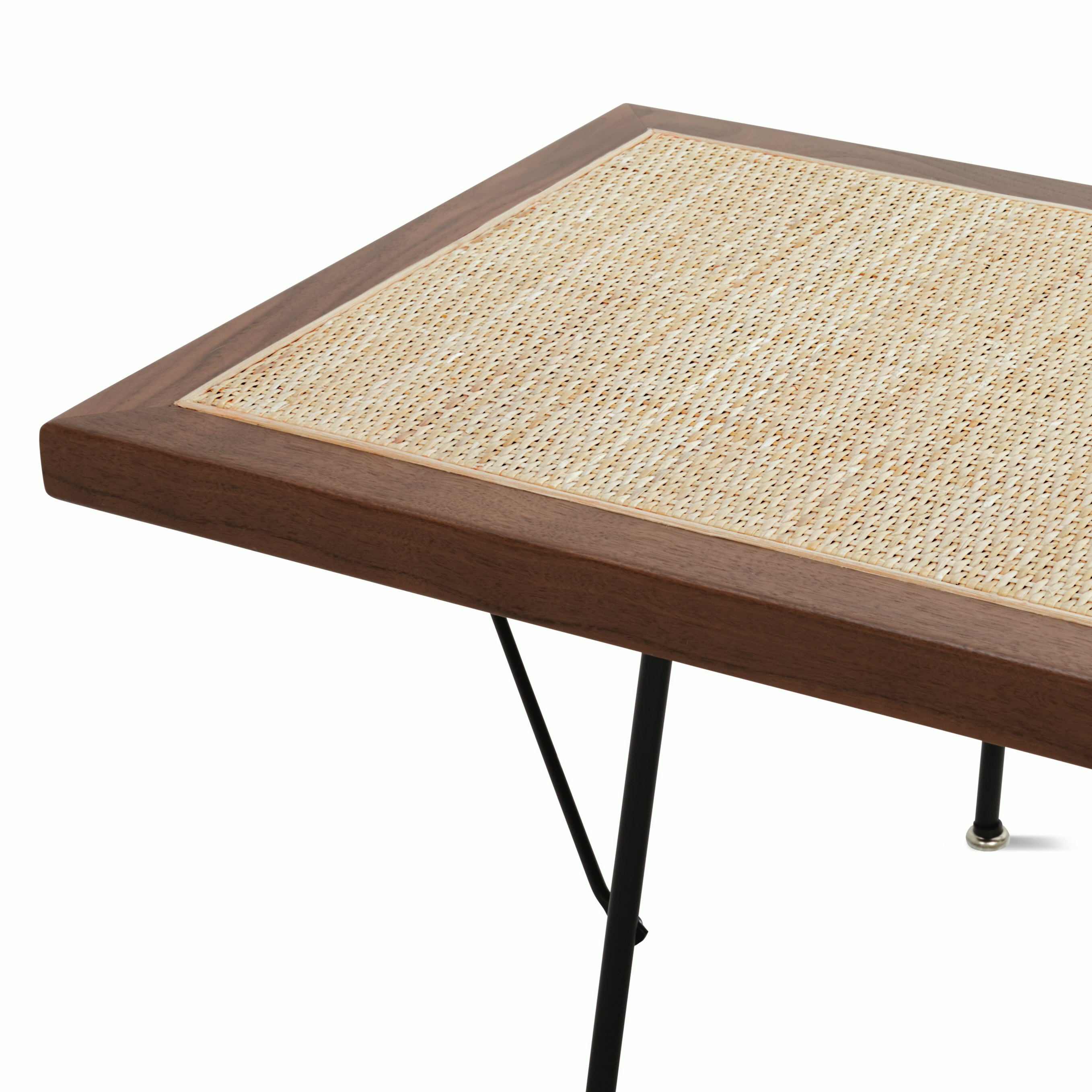 A close up detail of the walnut frame, cane detailing, and black metal legs of the Nelson Cane Bench.