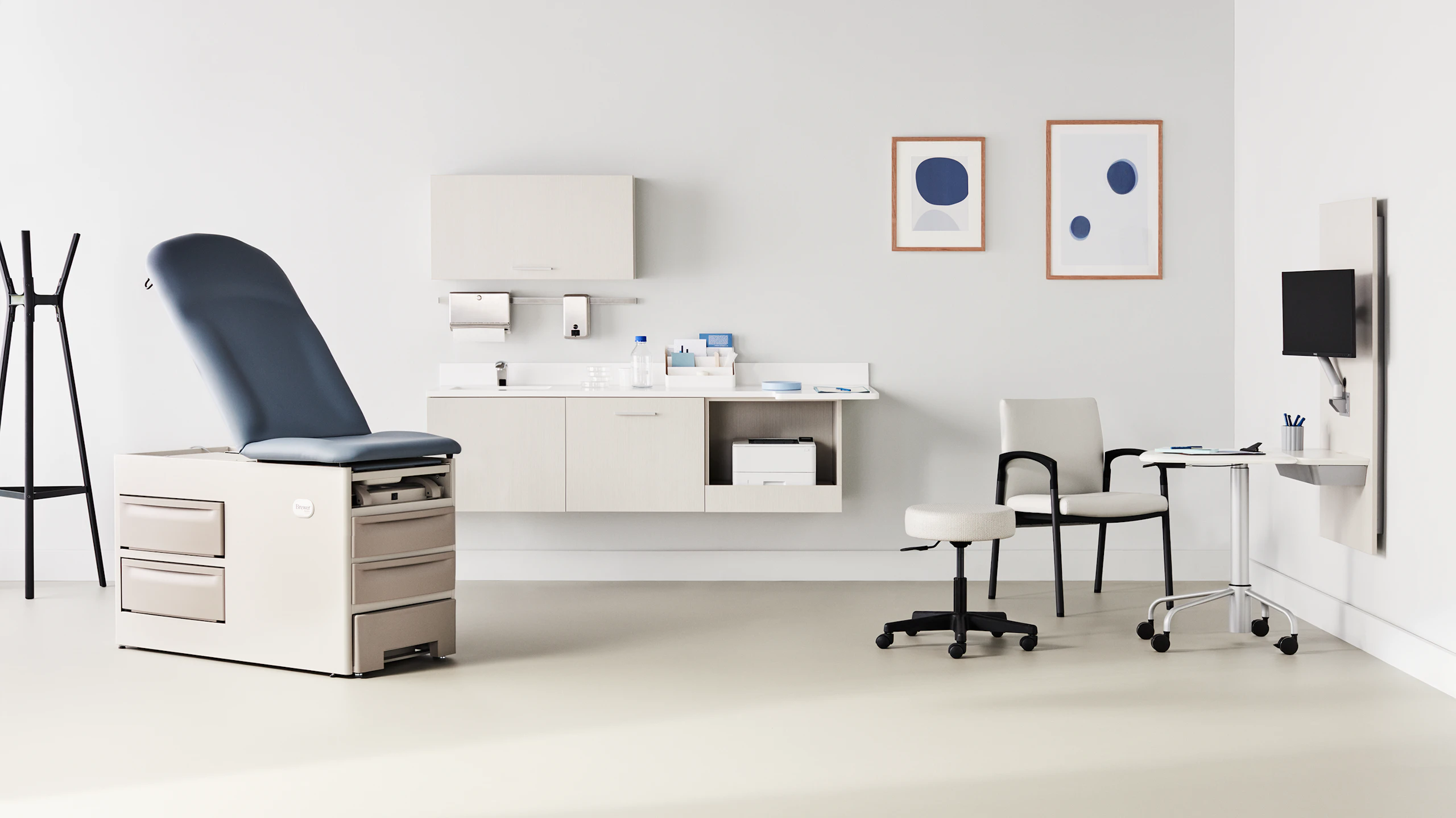 Exam room with a Brewer Company exam table in a soft white base and a blue upholstered back and seat with Mora casework in a light wood laminate on the back wall and Intent solution wall in a light wood laminate to the side that includes a mobile, height-adjustable table and is surrounded by a Valor side chair in a light gray upholstery and black base and a physician stool.