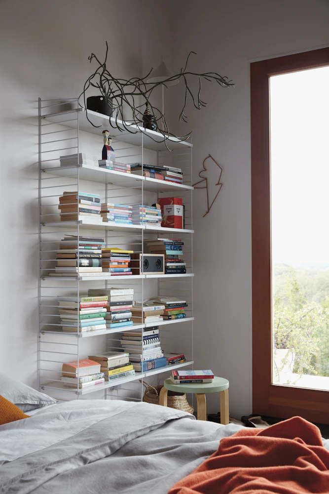 Tall white shelving unit filled with books in bedroom
