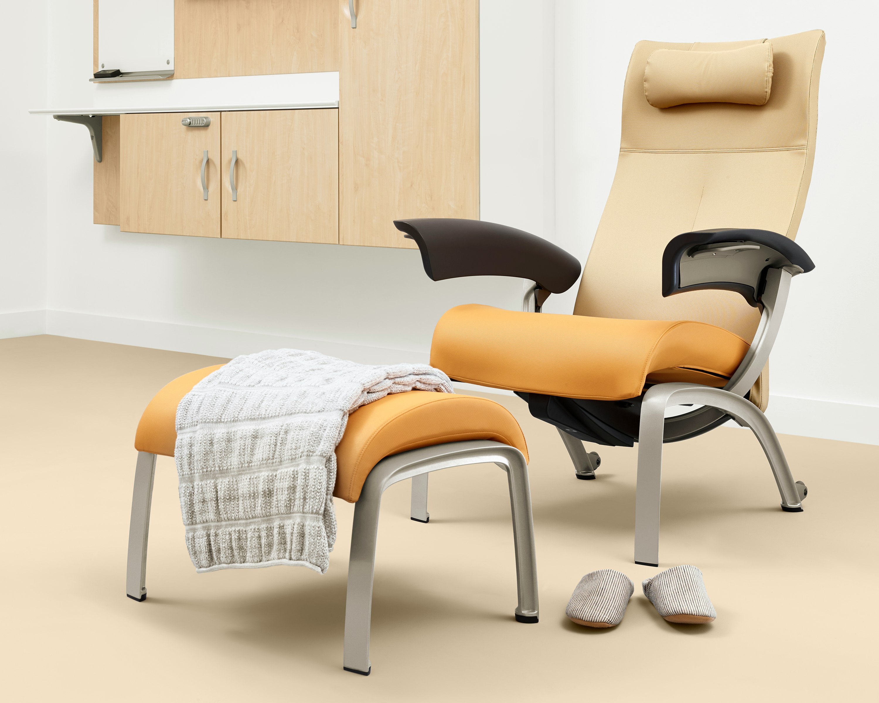 A patient room with a Nemschoff Nala Patient Chair and Ottoman upholstered in multiple fabrics with dark brown arms with Compass System casework on the wall.