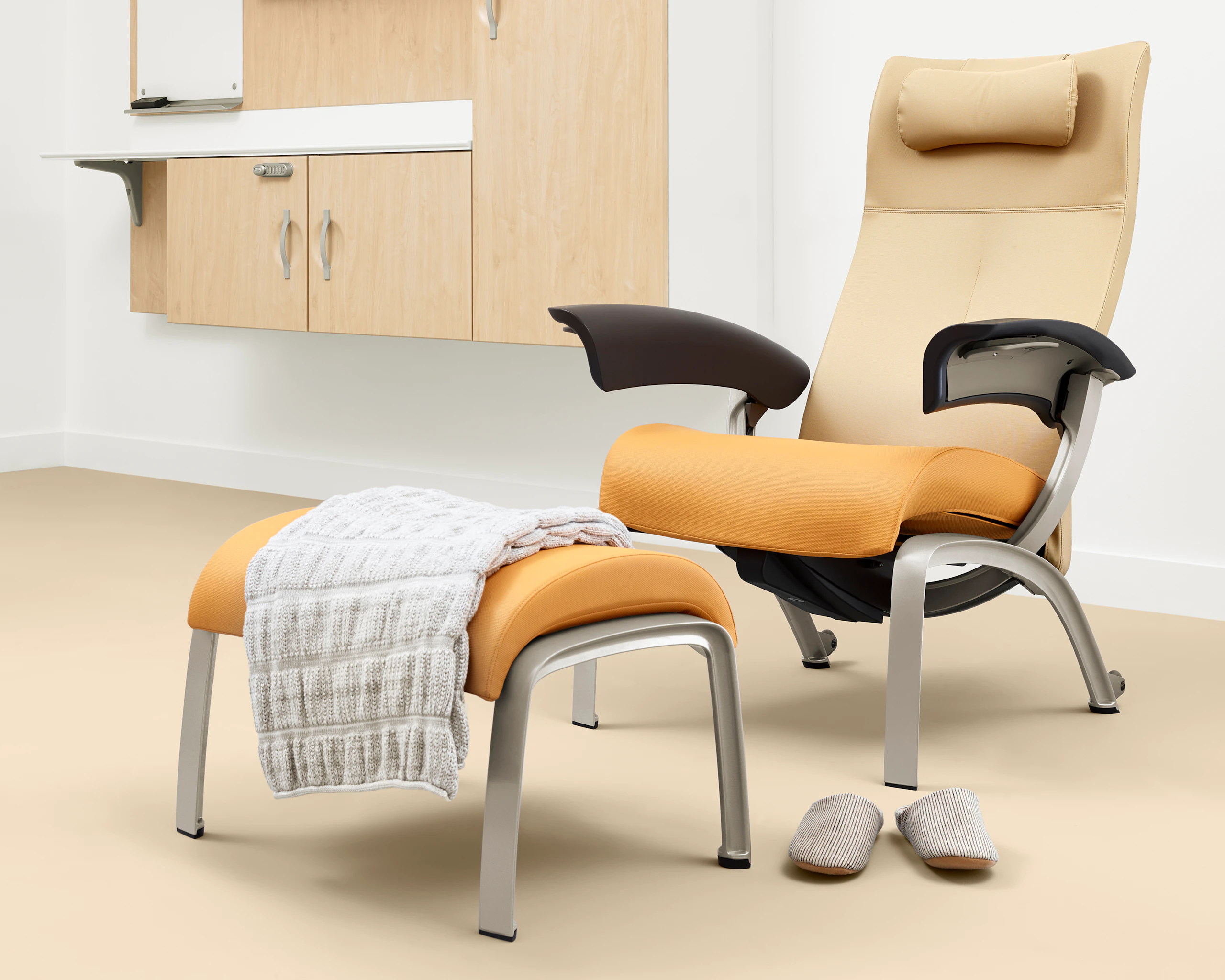 A patient room with a Nemschoff Nala Patient Chair and Ottoman upholstered in multiple fabrics with dark brown arms with Compass System casework on the wall.