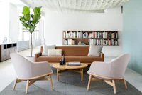 A lounge area featuring a brown Wood Base sofa, two light gray Reframe mid-back lounge chairs, and a round Reframe occasional table.