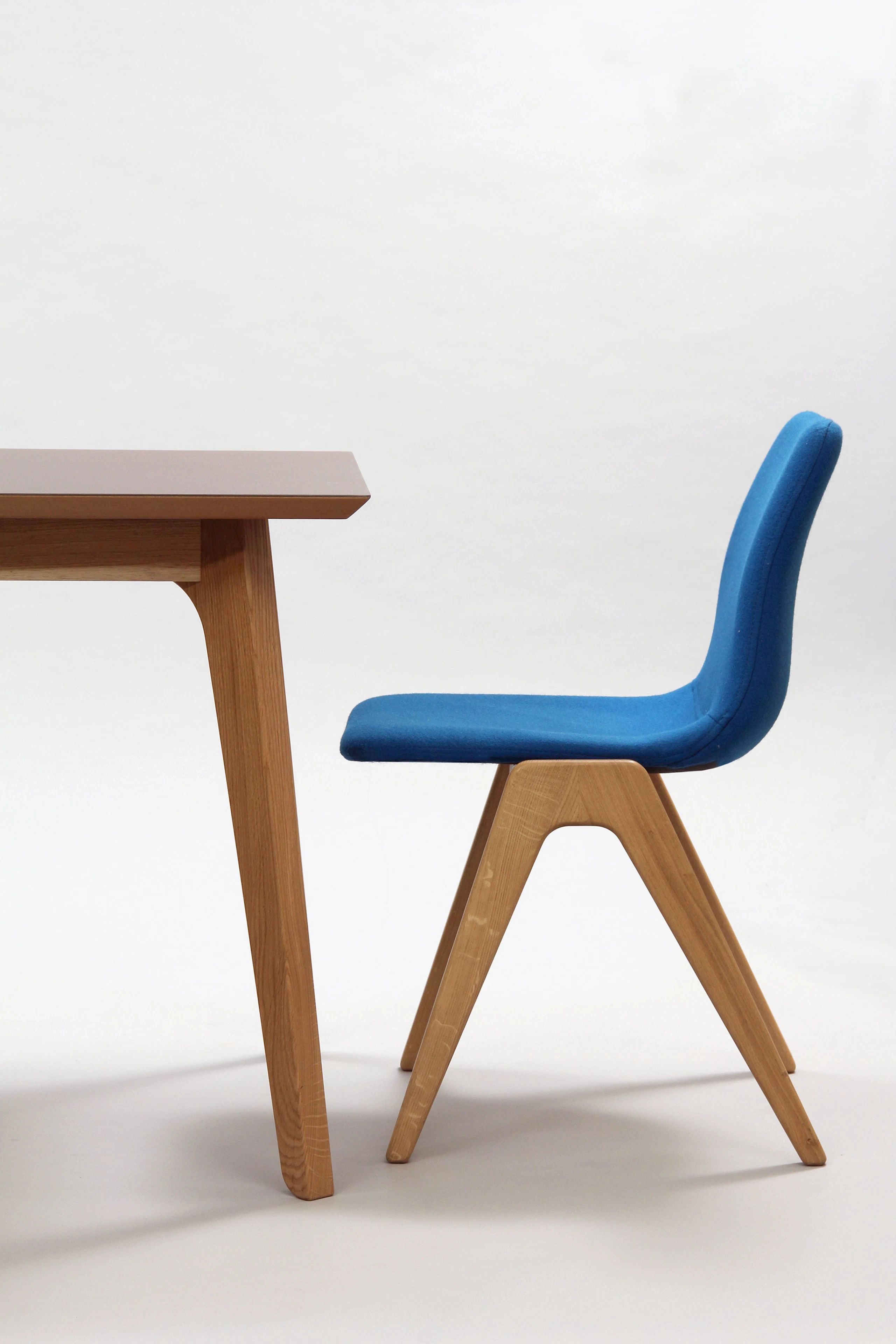A side view of a blue Viv Wood Chair sitting at the end of a naughtone Dalby Conference Table.