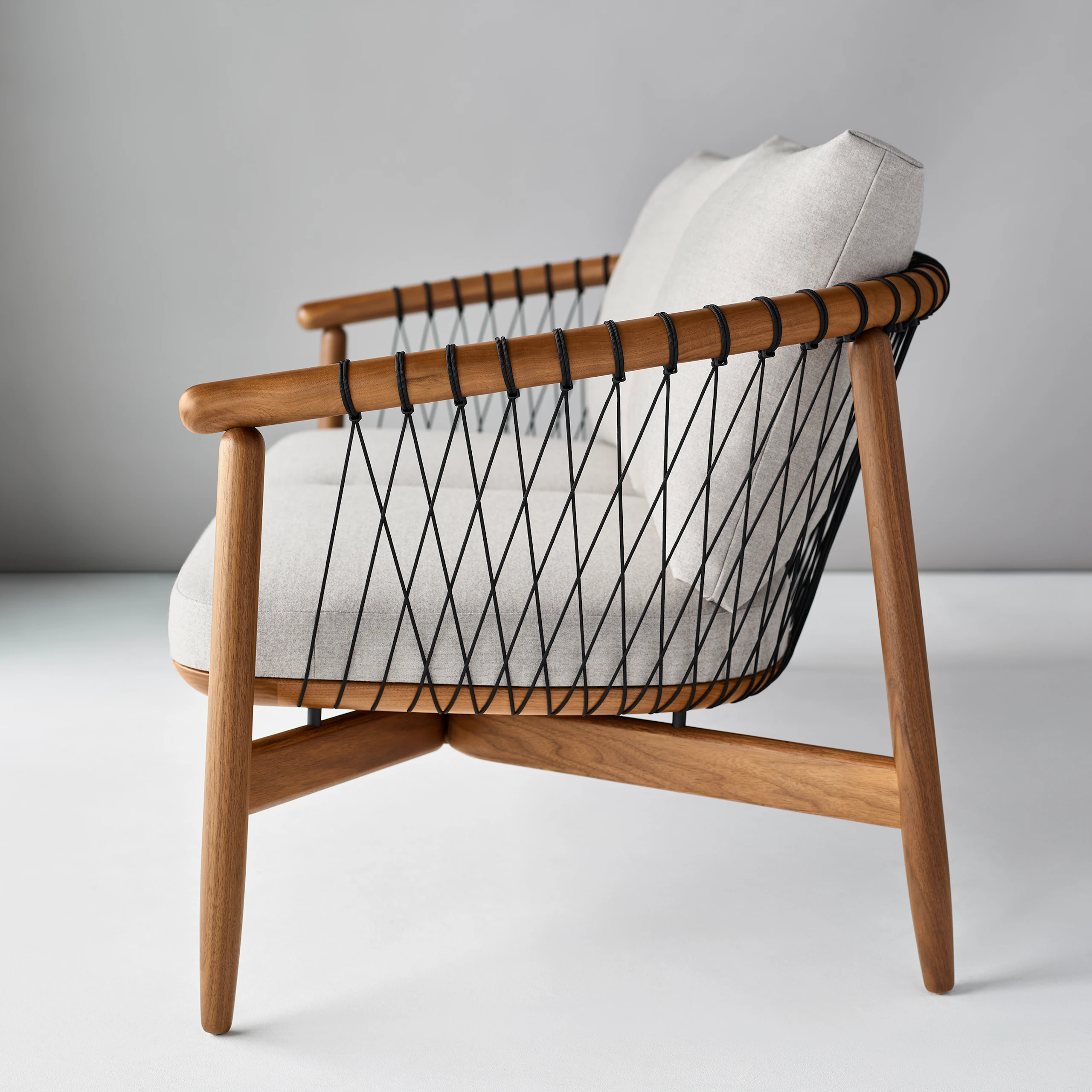 A Crosshatch Settee with a walnut frame, black cords, and light neutral fabric. Viewed from the side.