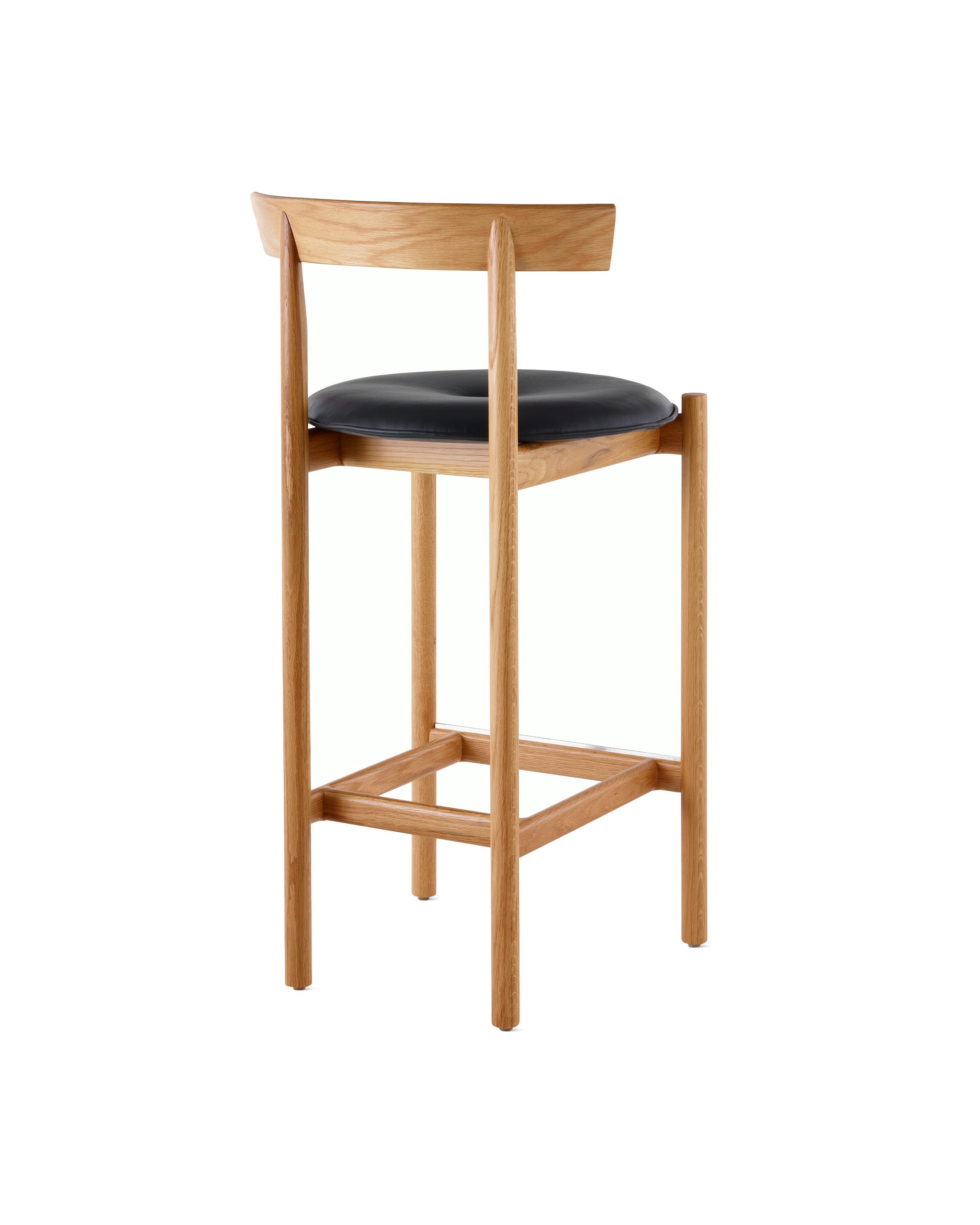 An oak Comma Stool with a seat pad, viewed from the back at an angle.