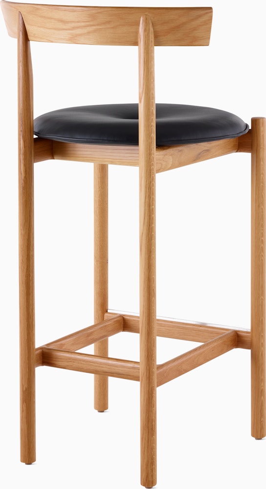 An oak Comma Stool with a seat pad, viewed from the back at an angle.