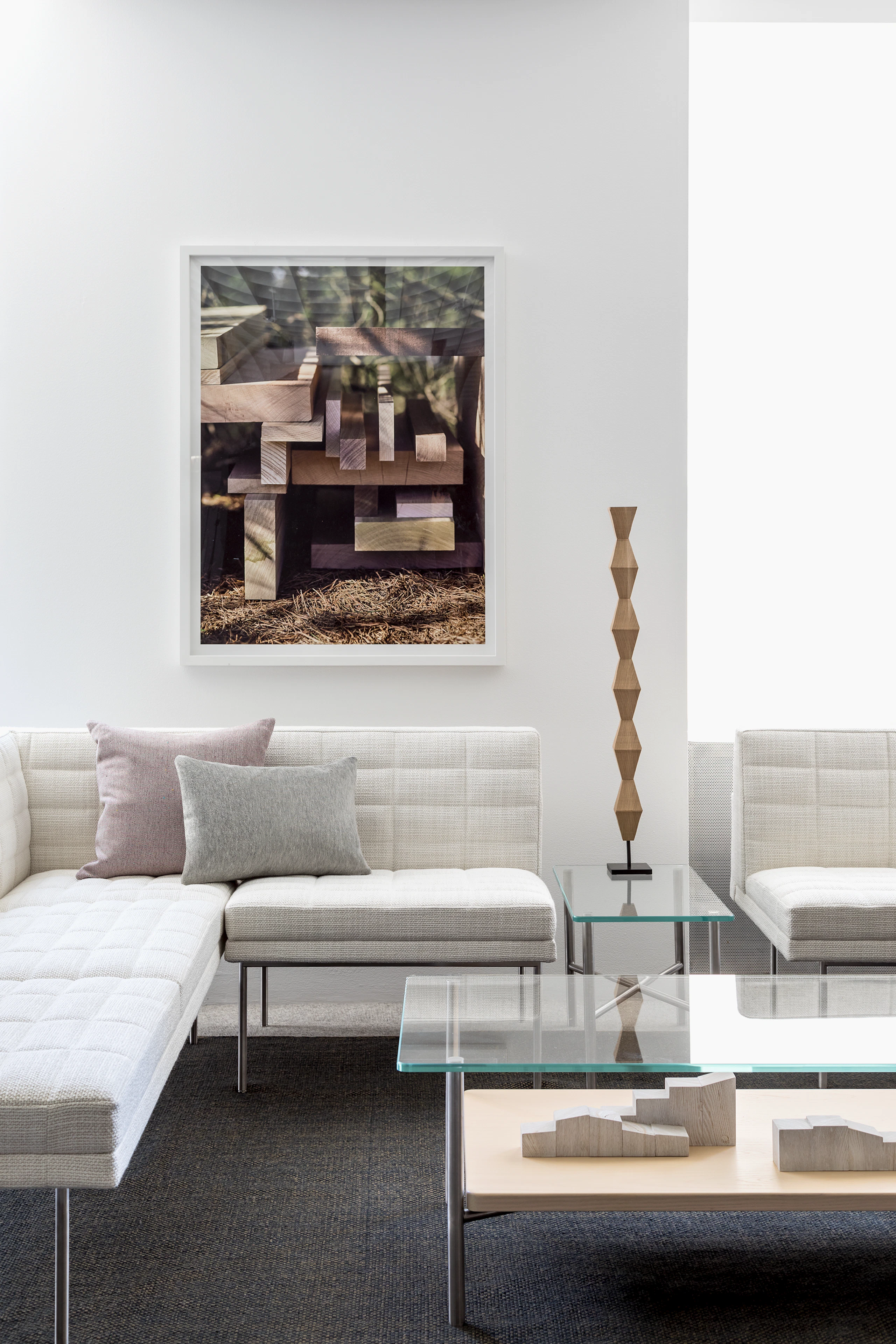 A lounge featuring a rectangular Layer coffee table with a glass top and wood shelf, complemented by off-white Tuxedo Component Lounge Seating.