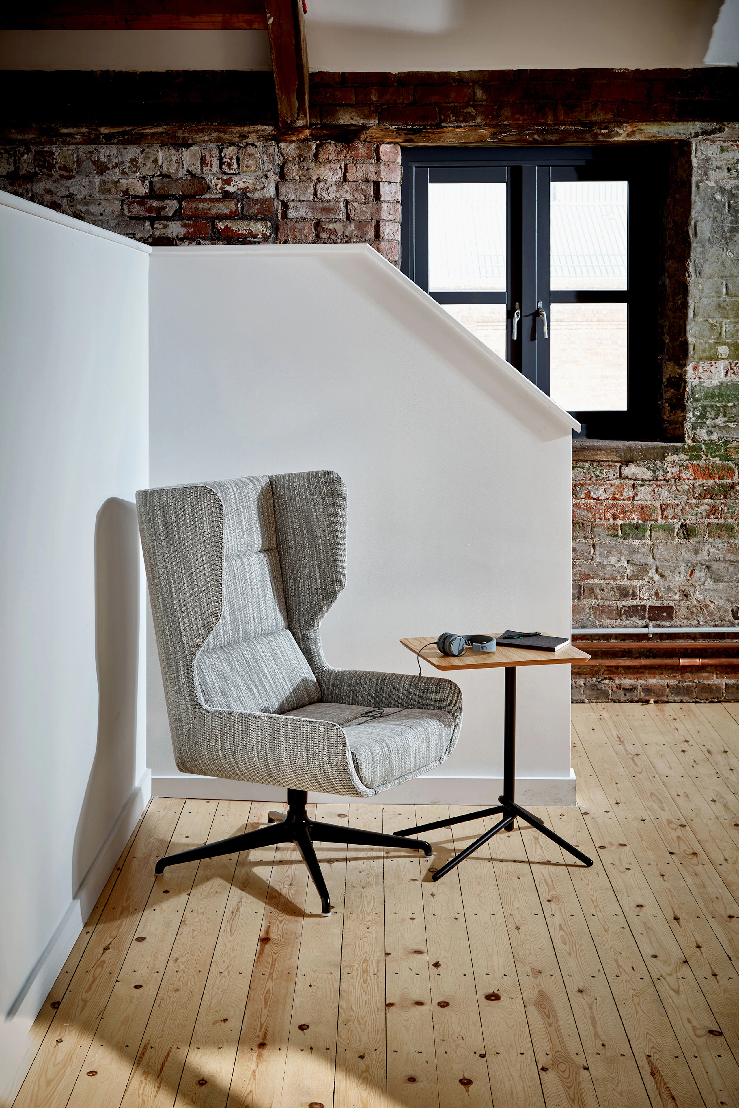 A light gray patterned naughtone Hush Chair seated in a corner with a Knot Side Table with oak top and black base.