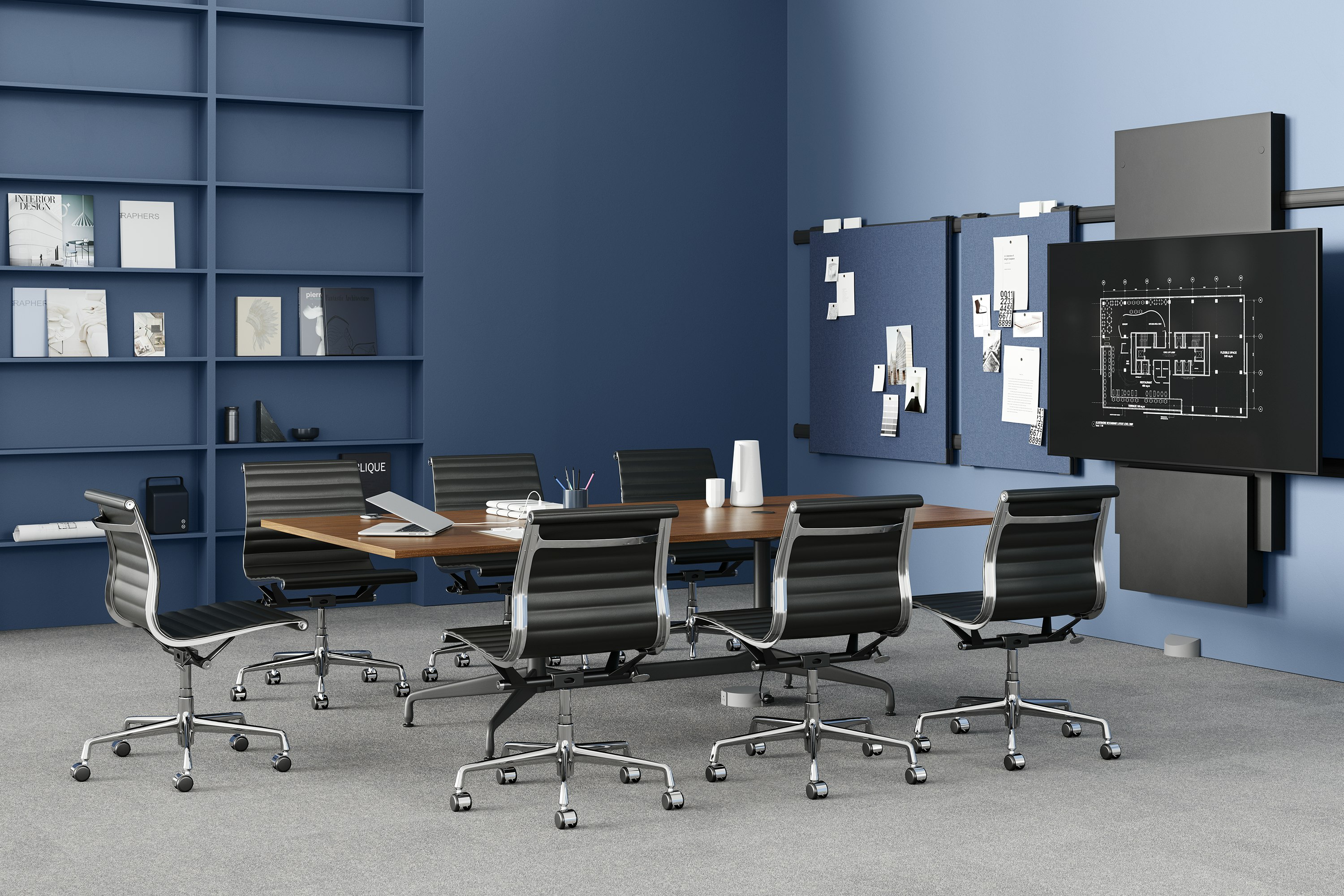A conference table, surrounded by seven black Eames Aluminum Group chairs, is positioned in front of a large monitor. The table is powered by a Logic Reach wall start.