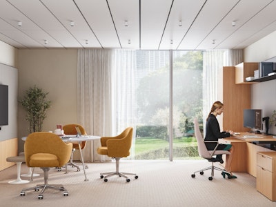 A person working at a computer in a private office setting furnished with Geiger Taper Chairs, a Knoll Grasshopper Table, Saarinen Executive Chairs and Saarinen Tulip Stools.