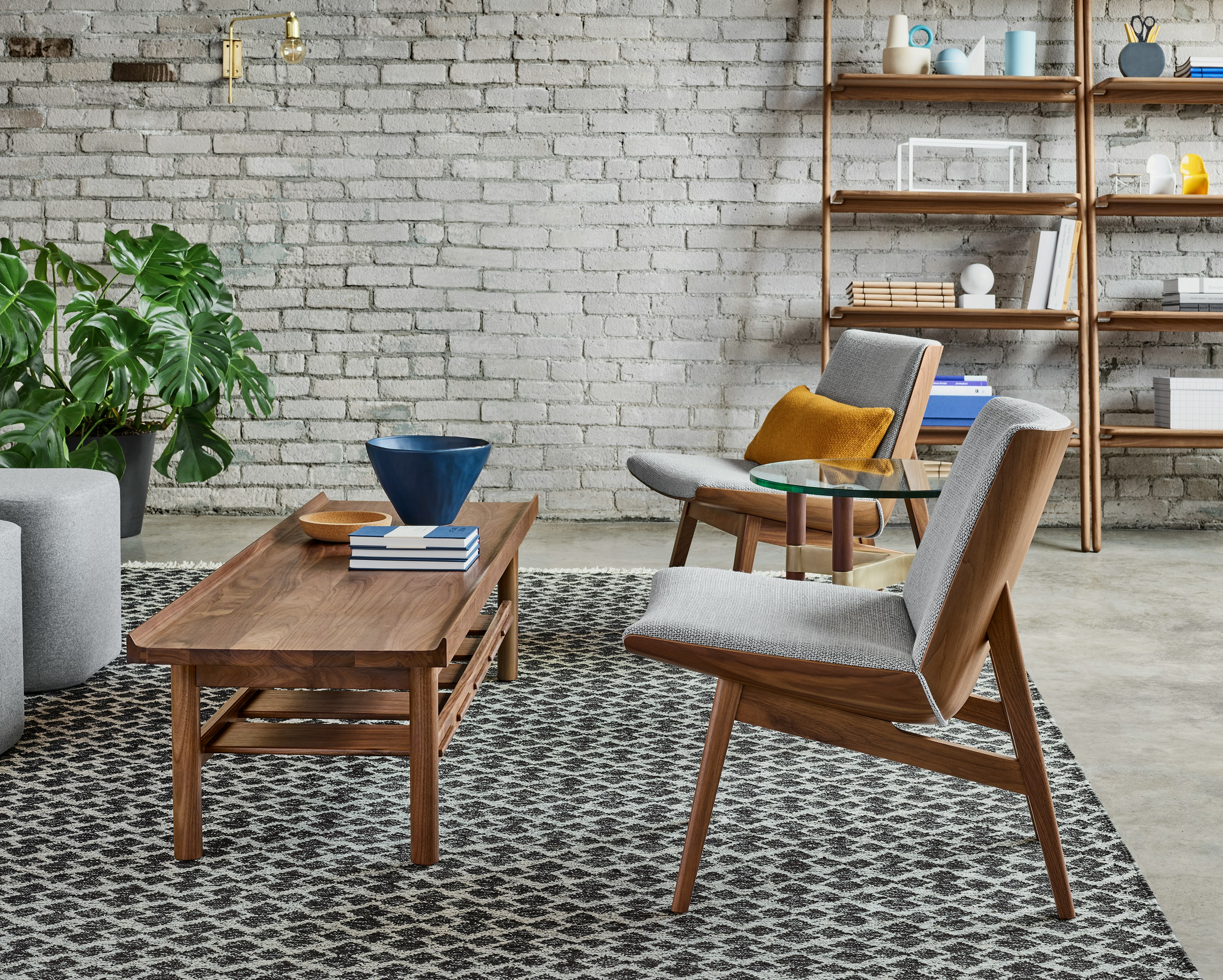 A lounge setting with two low back Clamshell Lounge Chairs with light gray cushions and walnut bases set around a Tamarack Table and Bench.