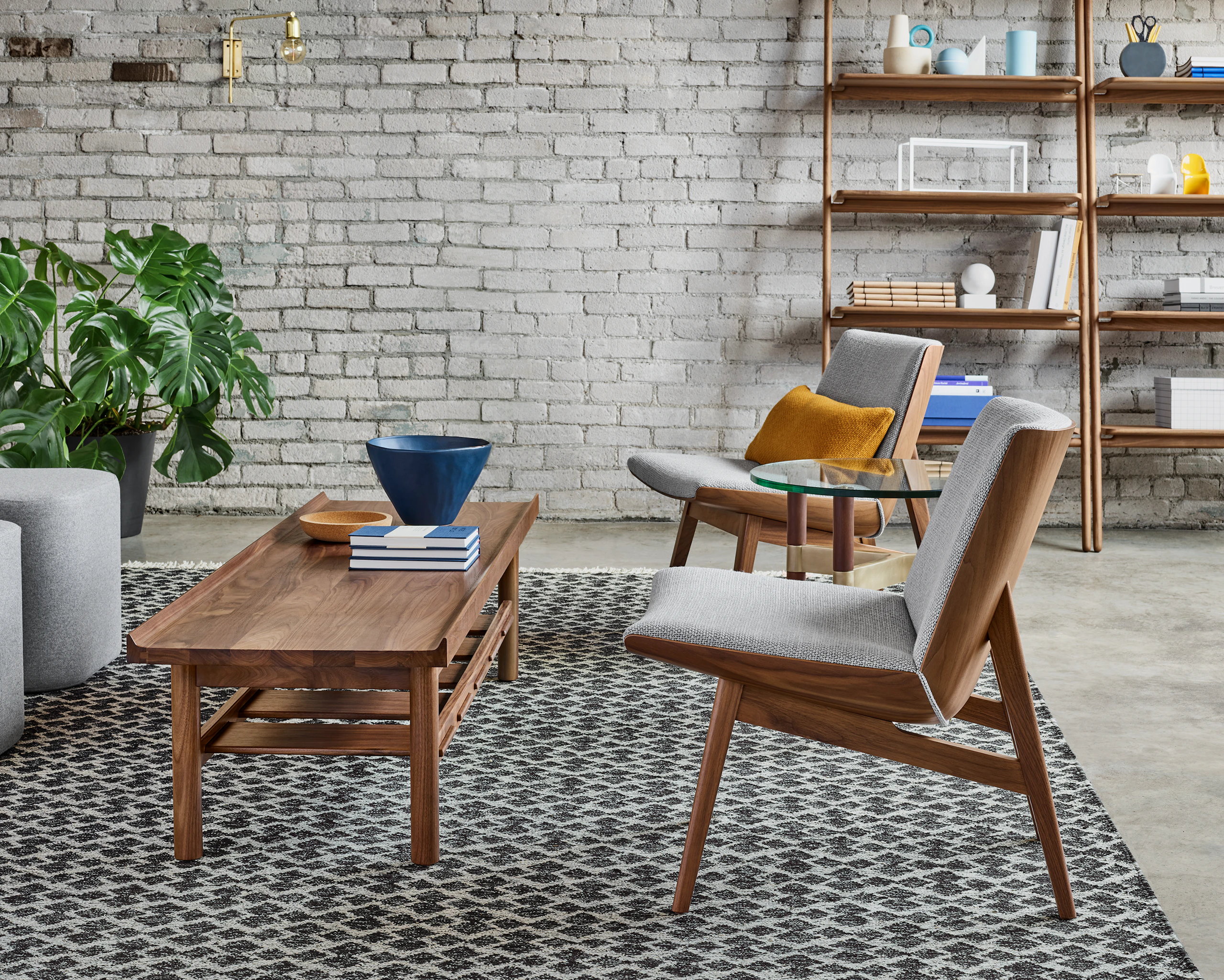 A lounge setting with two low back Clamshell Lounge Chairs with light gray cushions and walnut bases set around a Tamarack Table and Bench.