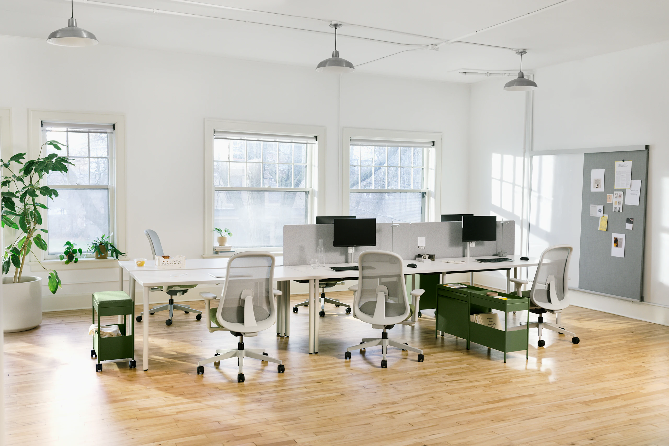 Six grey OE1 Rectangular Tables joined together to form a bench with green OE1 Storage Trolleys, green Lino Chairs and an OE1 Wall Rail and Board in the background.