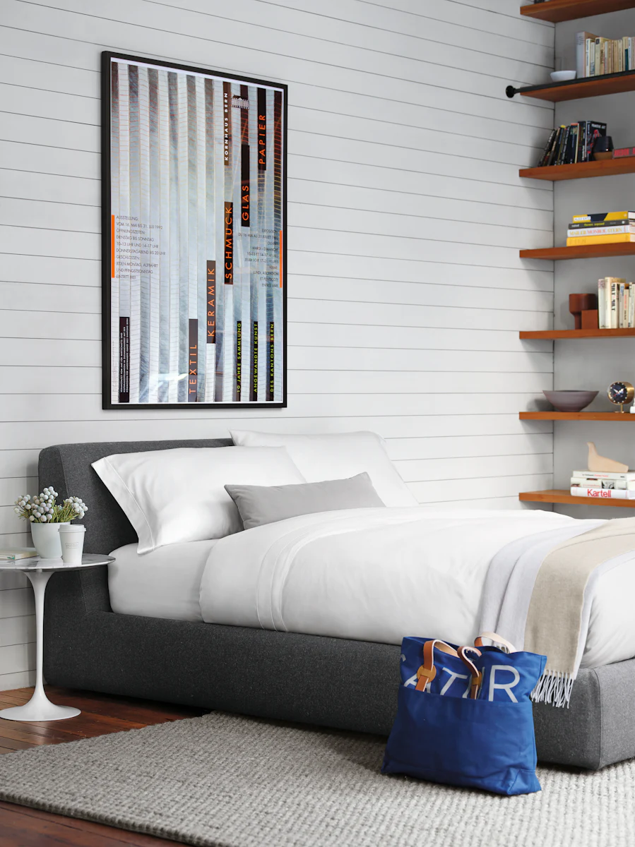 Low platform bed with a white duvet and colorful folded blankets stored underneath