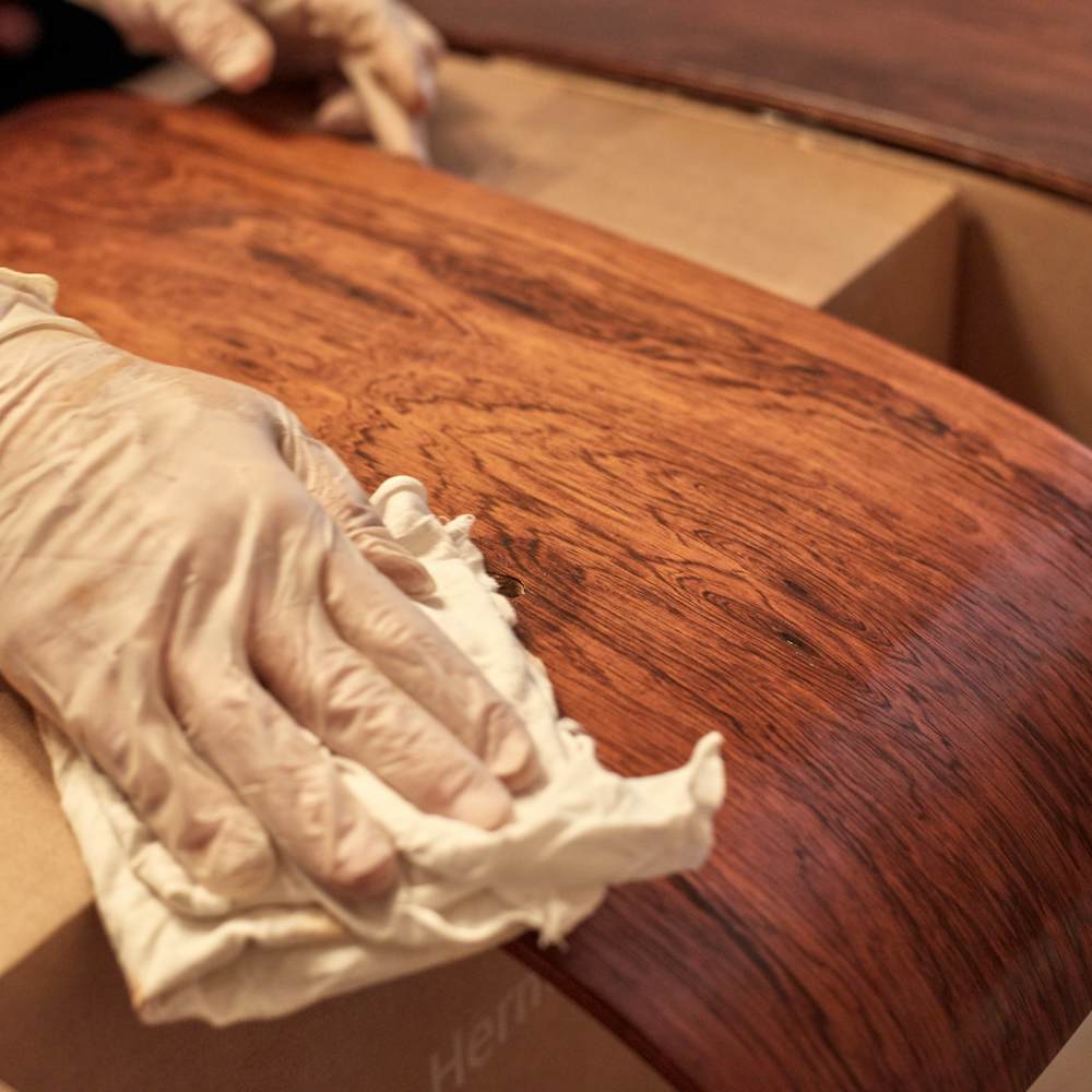 The hand of a person rubbing stain on the shell of an Eames Lounge Chair.