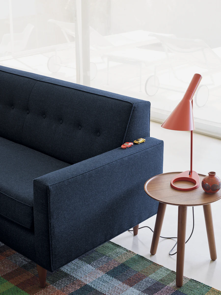 Blue sofa with a round wooden side table and orange desk lamp beside it.